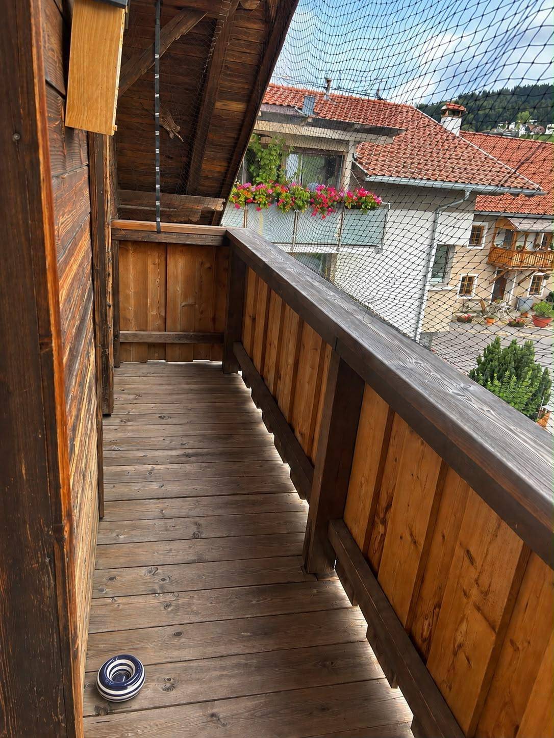 Rustikaler Holzbalkon mit Sicherheitsnetz und Blick auf die umliegenden Häuser und Hügel.