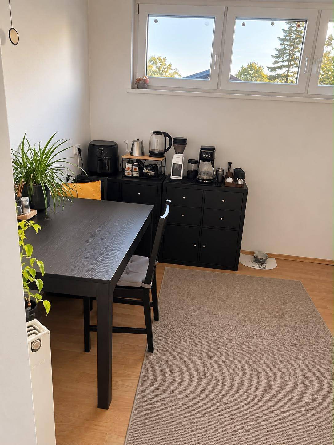 Essbereich mit dunklem Holztisch, Stühlen und einer Kaffeestation unter dem Fenster.