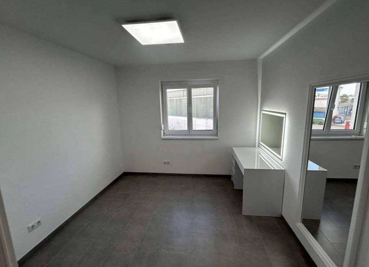 Helles Zimmer mit Fliesenboden, großem Spiegel und beleuchtetem Schminktisch.