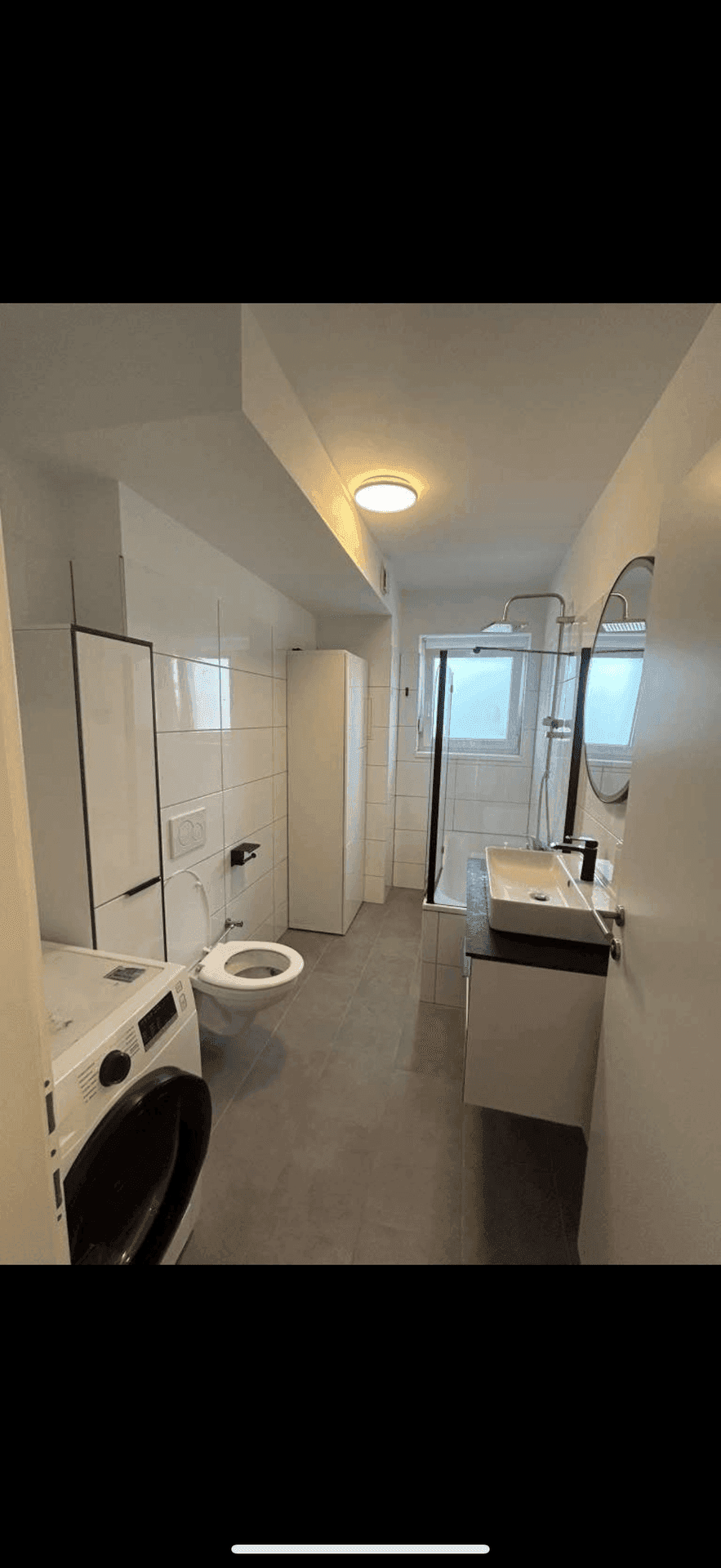 Modernes Badezimmer mit Toilette, Waschbecken, Dusch-Badewannen-Kombination und Waschmaschine.