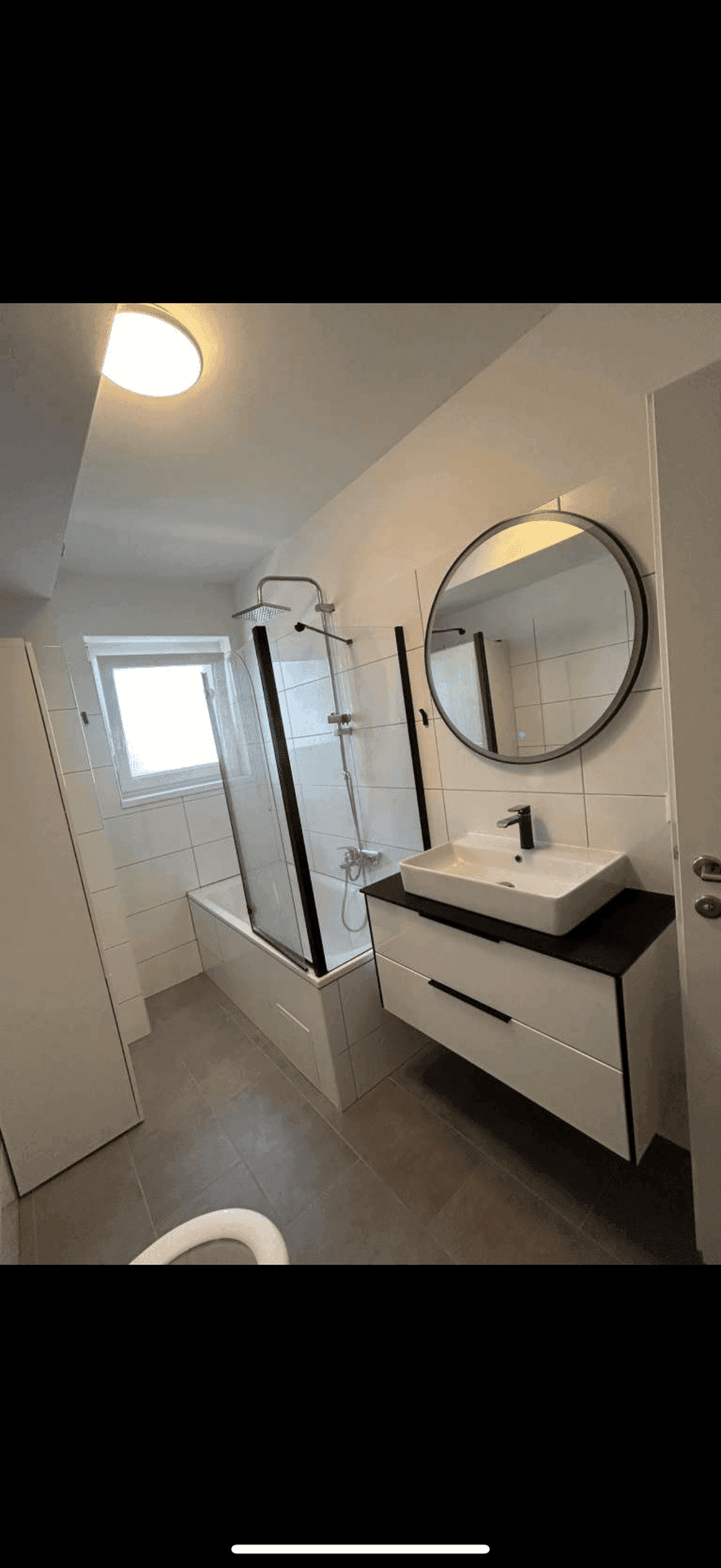 Helles Badezimmer mit modernem Waschbecken, Spiegel und Dusch-Badewannen-Kombination.