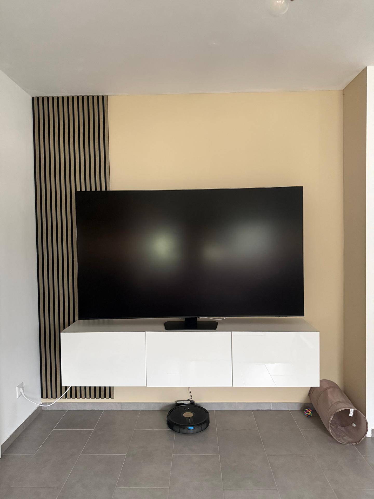 Wohnzimmer mit großem Fernseher, schwebendem TV-Möbel und dekorativer Wandverkleidung.