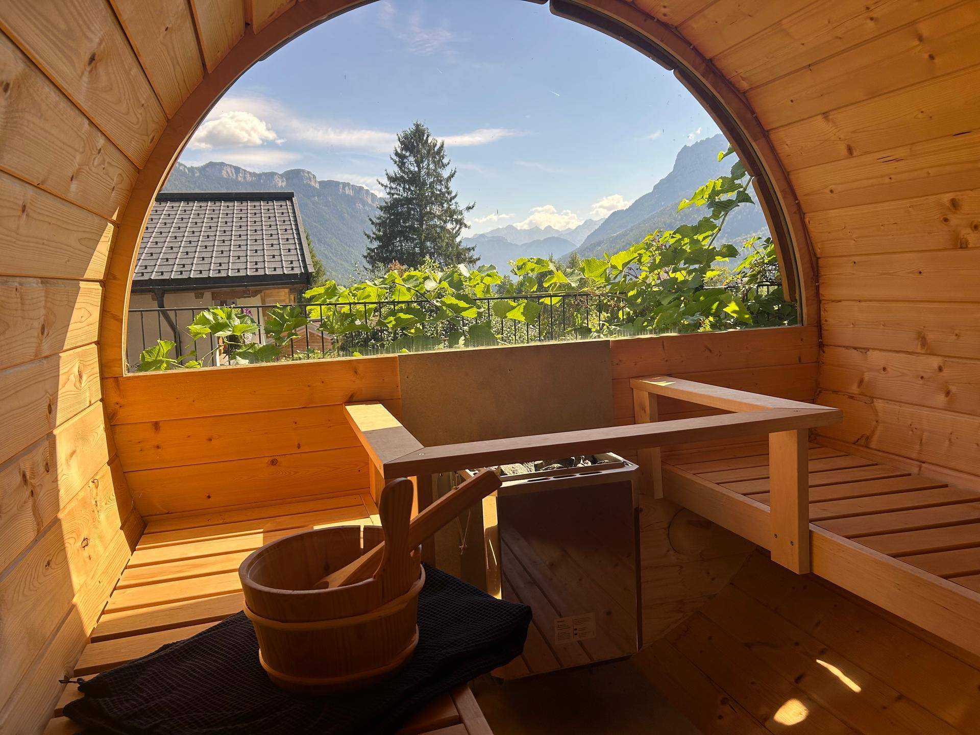 Innenansicht einer Fasssauna mit Holzbänken und Panoramafenster mit atemberaubendem Bergblick.