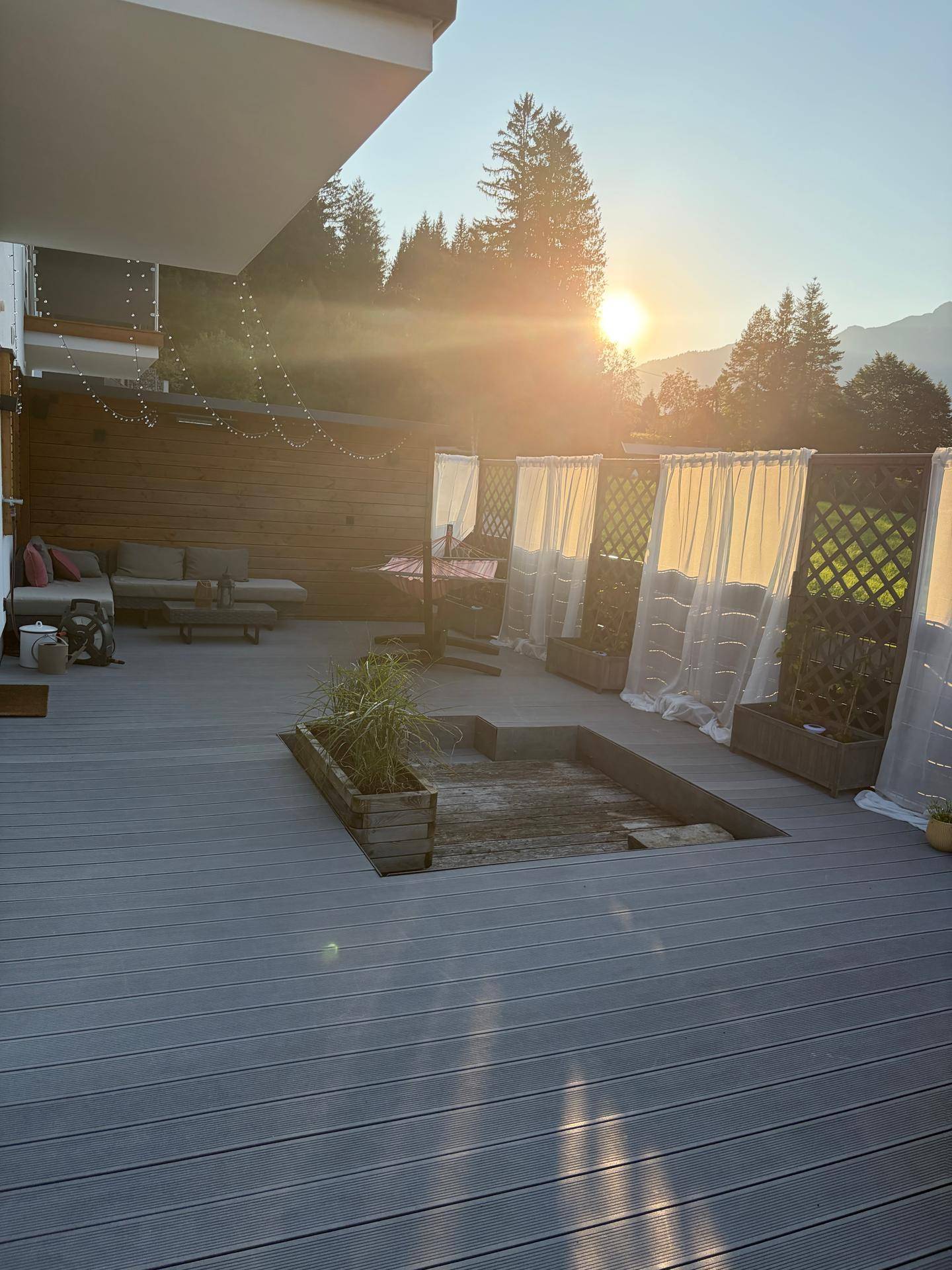 Große Terrasse mit Holzverbunddielen, integriertem Wasserbecken und gemütlicher Sitzecke bei Sonnenuntergang.