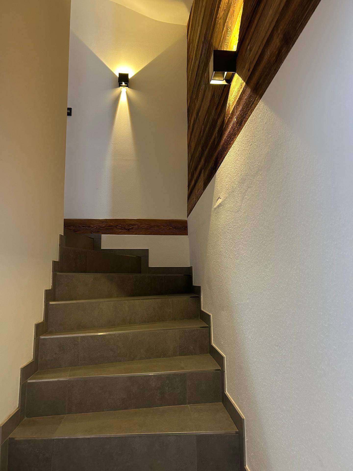 Moderne Treppe mit grauen Fliesenstufen und einer Holzakzentwand, die nach oben führt.