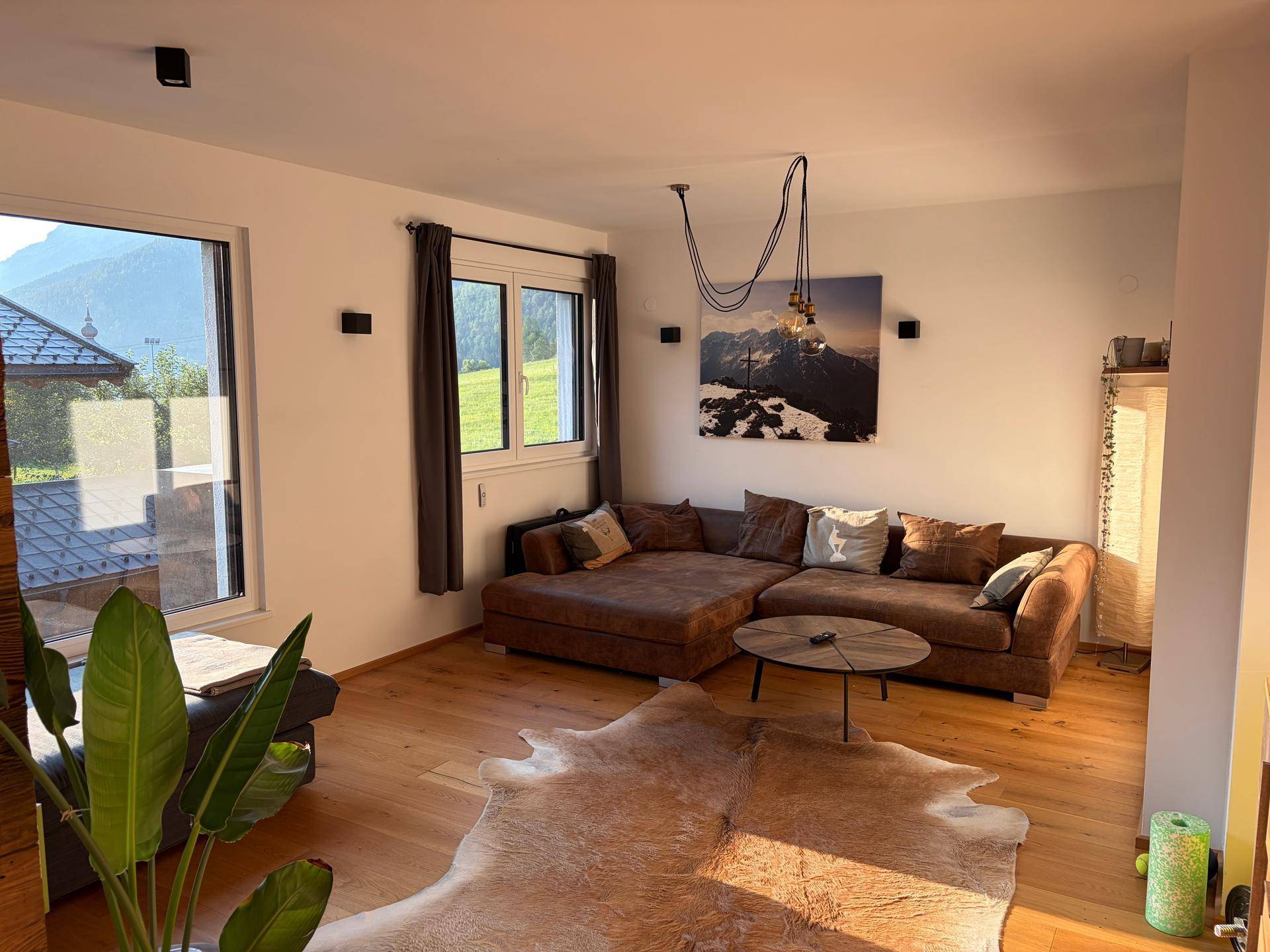 Geräumiges Wohnzimmer mit großem braunem Ecksofa, Couchtisch und Blick ins Grüne durch die Fenster.