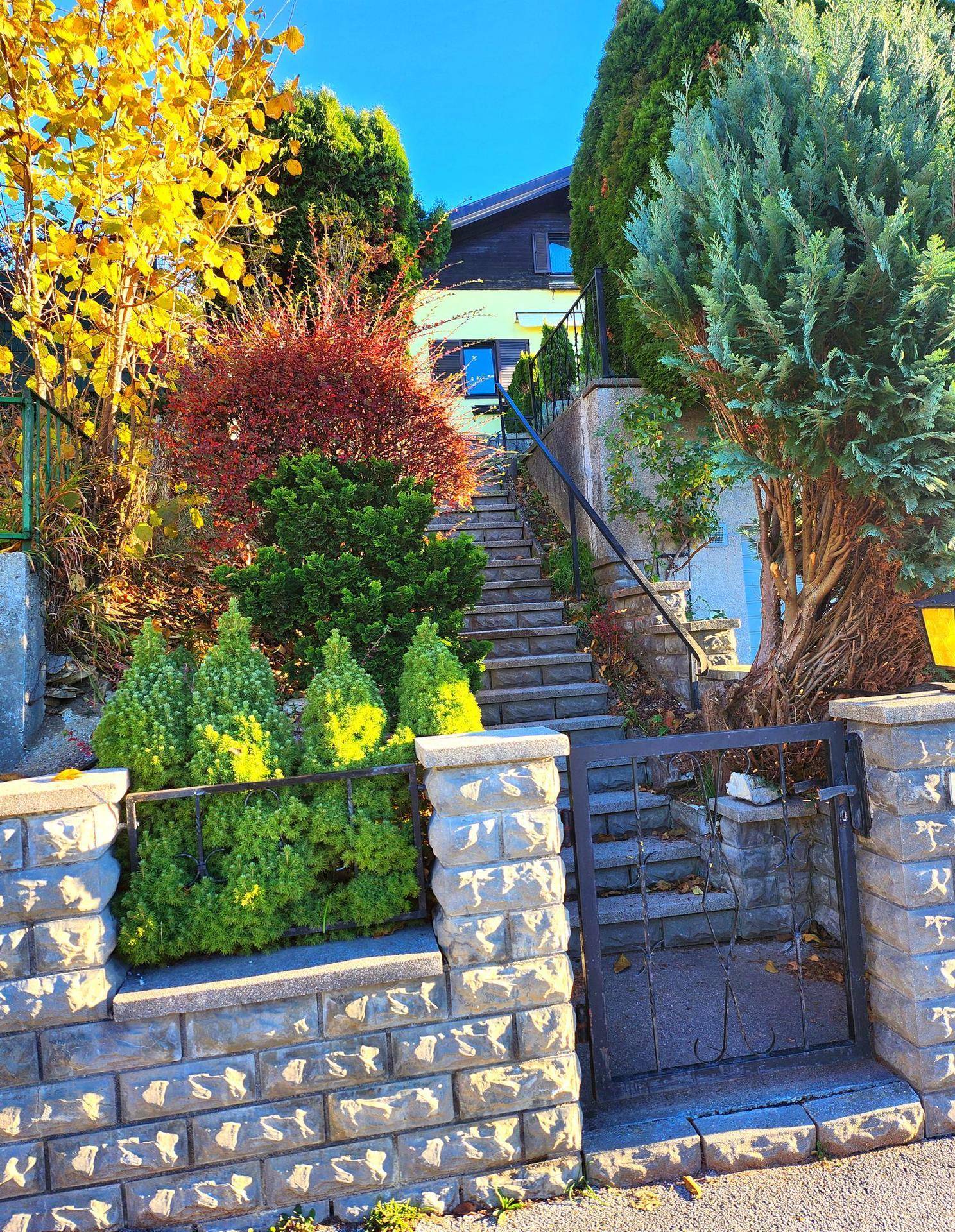 Steintreppe und Gartentor führen durch farbenfrohe Herbstbepflanzung zum Haus.