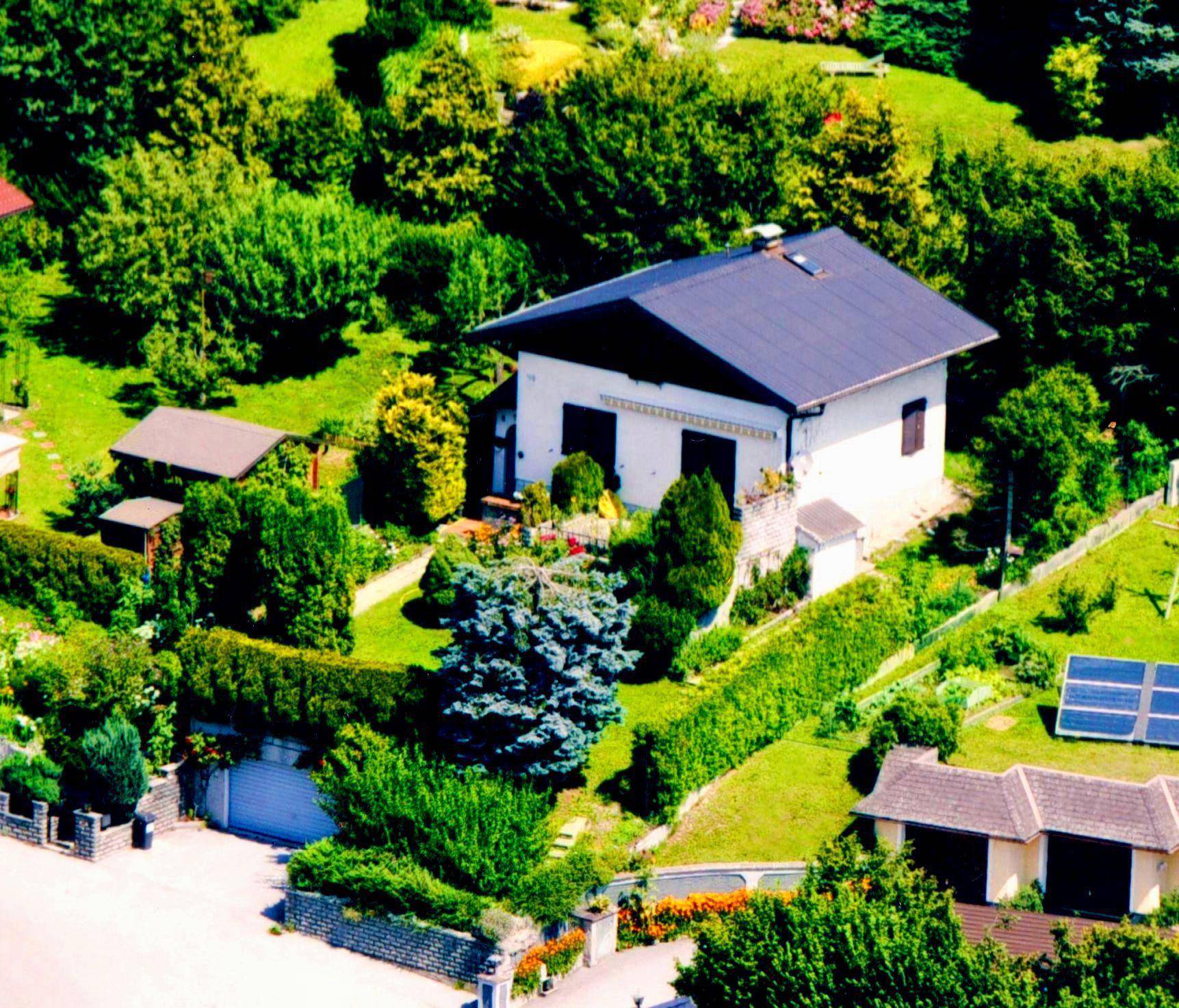 Luftaufnahme eines Einfamilienhauses mit großem Garten und umliegender grüner Landschaft.