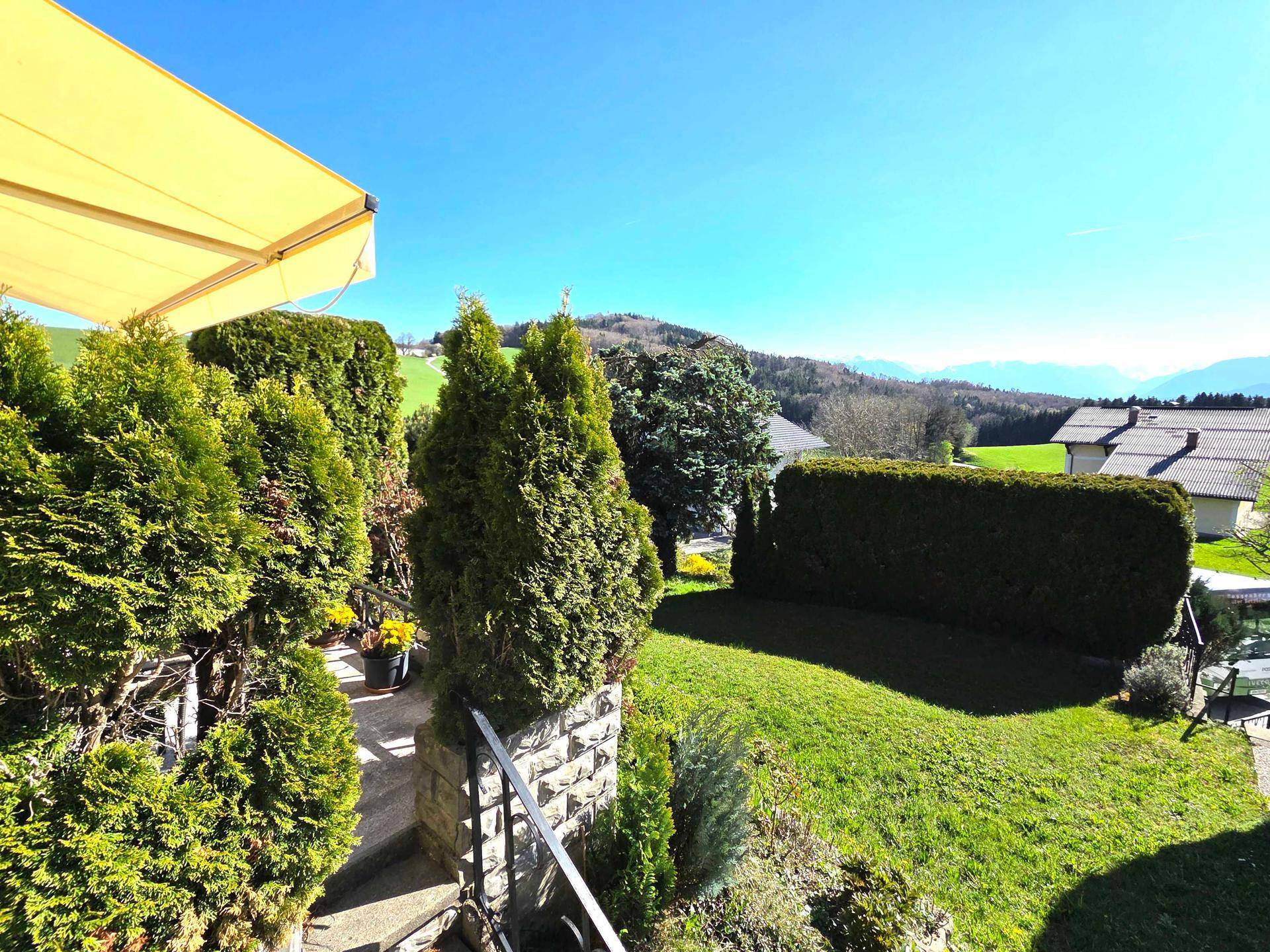 Sonniger Gartenbereich mit Hecken und weitem Blick auf die grüne Hügellandschaft.