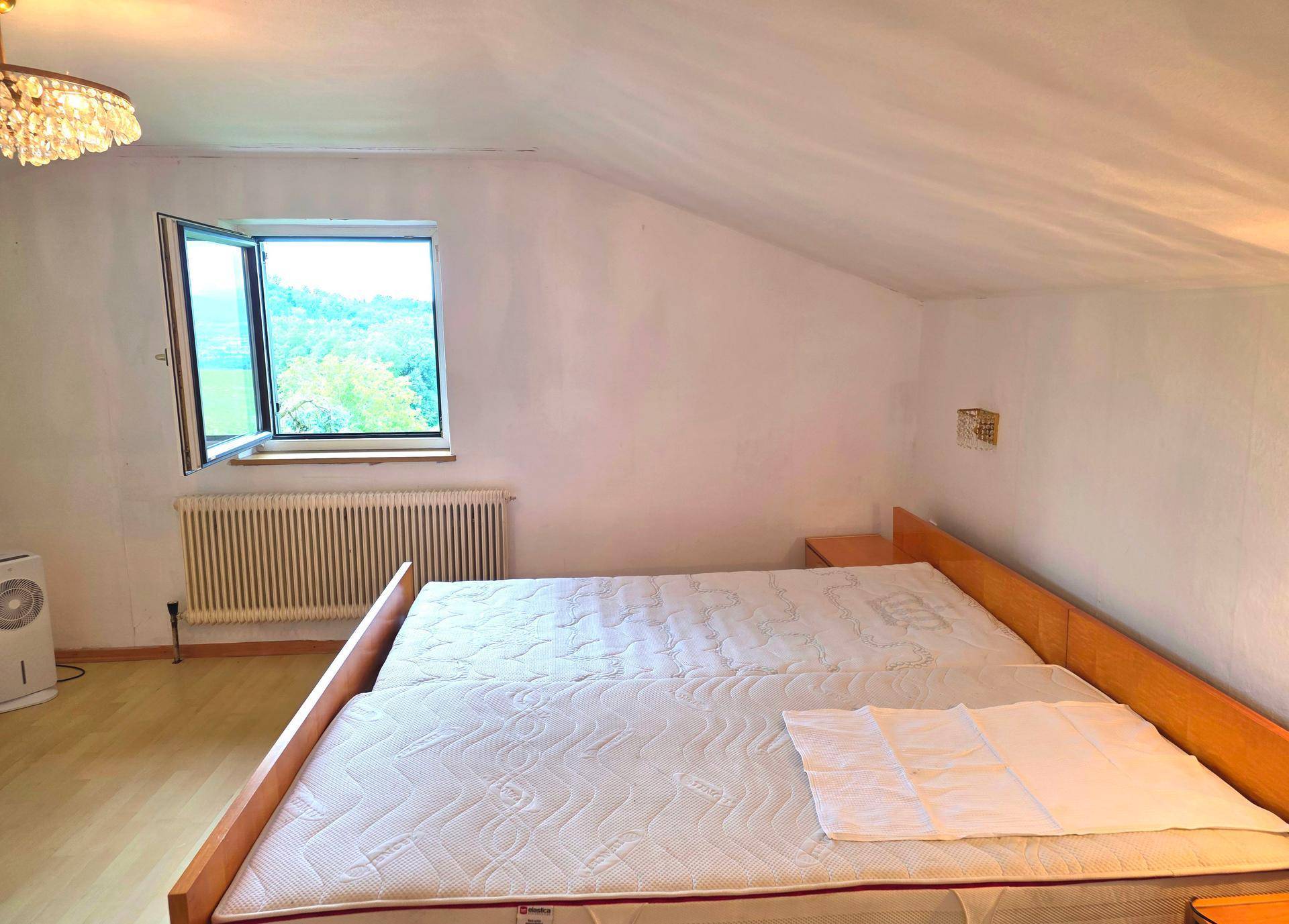 Schlafzimmer mit Doppelbett, Holzboden und Dachschräge, mit offenem Fenster und Heizkörper.