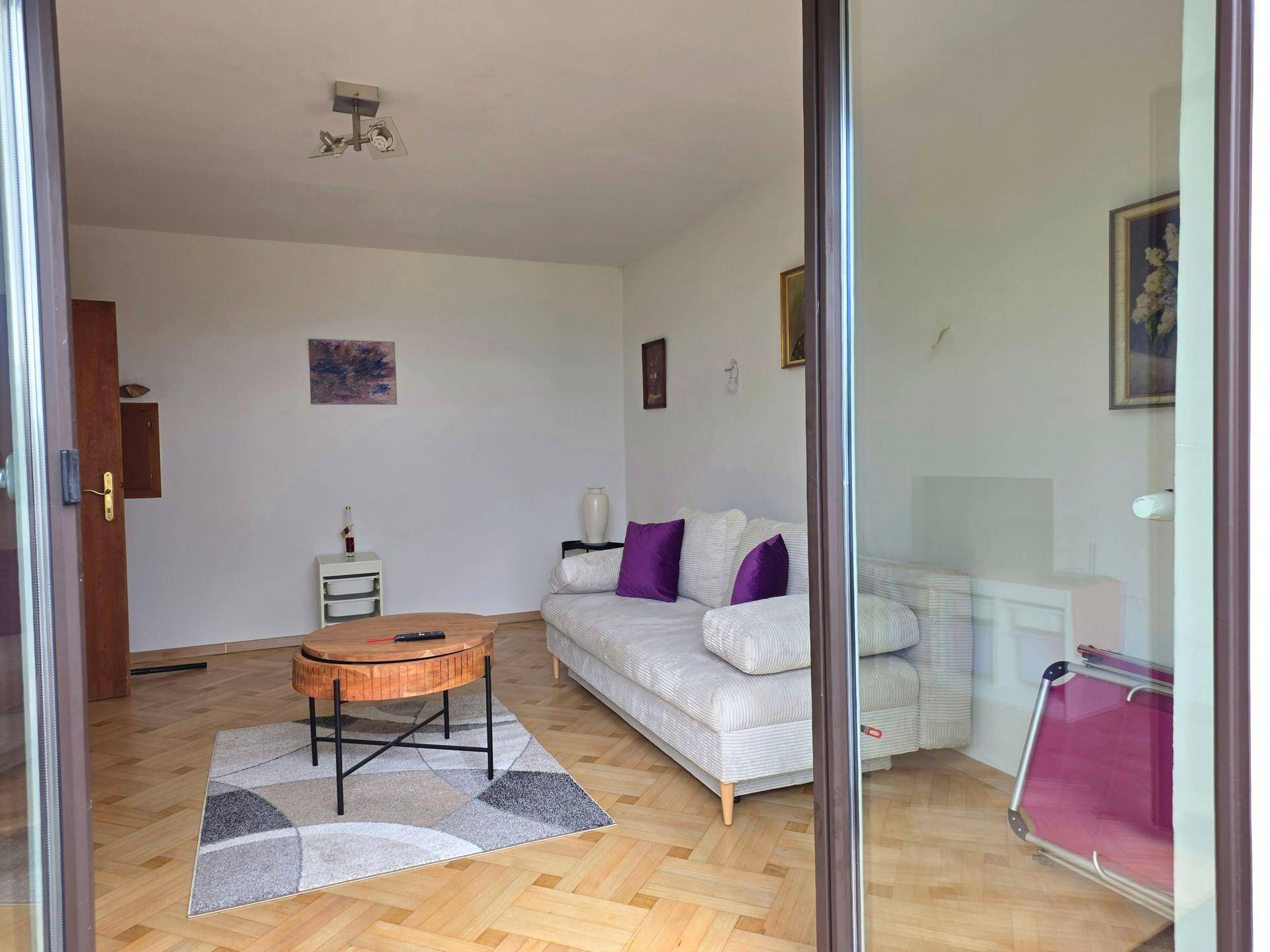 Helles Wohnzimmer mit Parkettboden, Sofa und einem Couchtisch, durch Glastüren sichtbar.