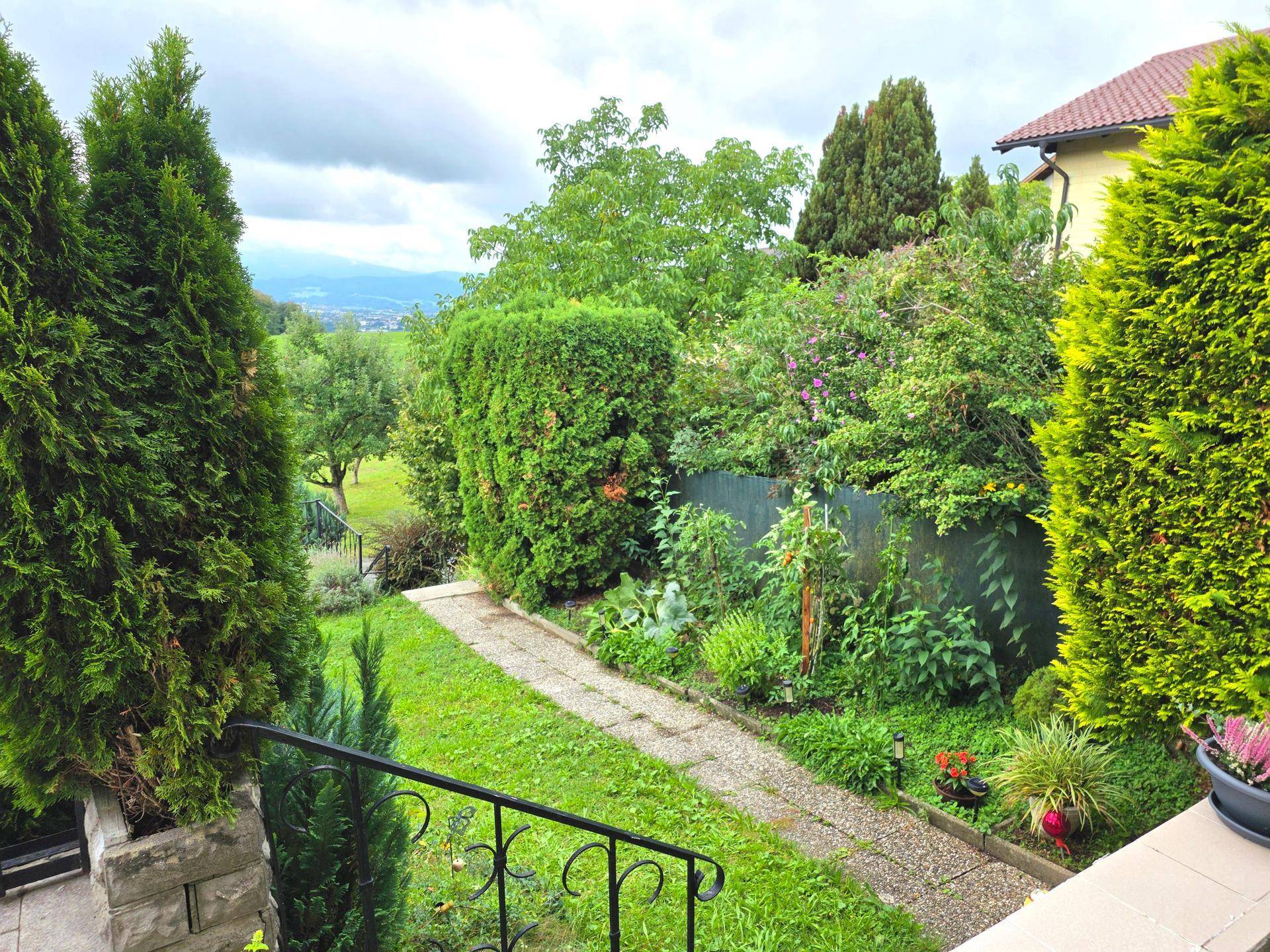 Gartenweg führt durch üppiges Grün mit hohen Bäumen und Sträuchern, umgeben von Natur.
