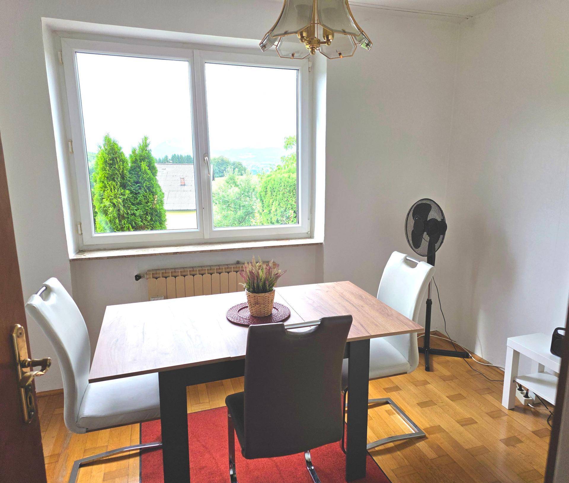 Essbereich mit Holztisch und Stühlen, hell durch ein großes Fenster mit Blick ins Grüne.