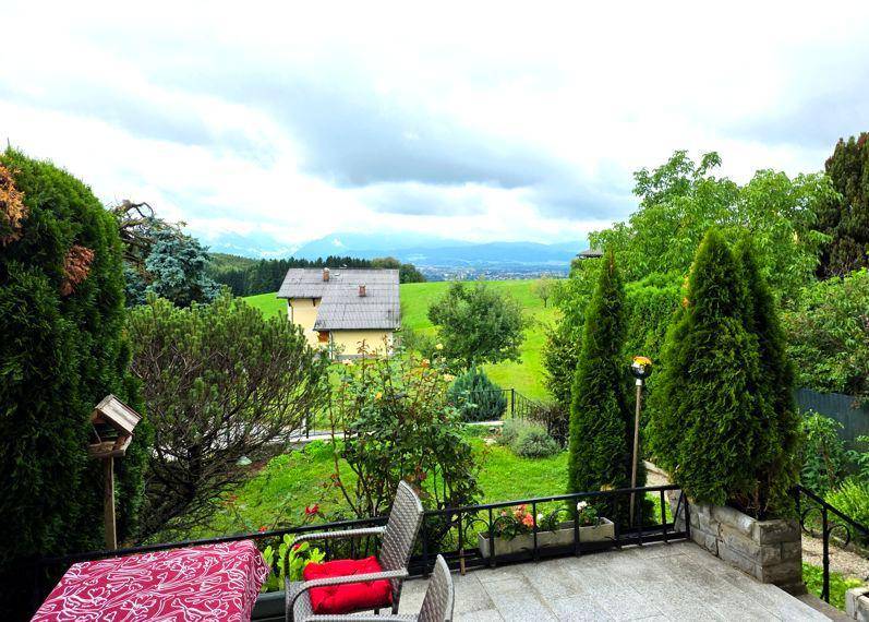 Terrasse mit Gartenmöbeln und weitem Blick über die grüne Landschaft und Berge unter bewölktem Himmel.