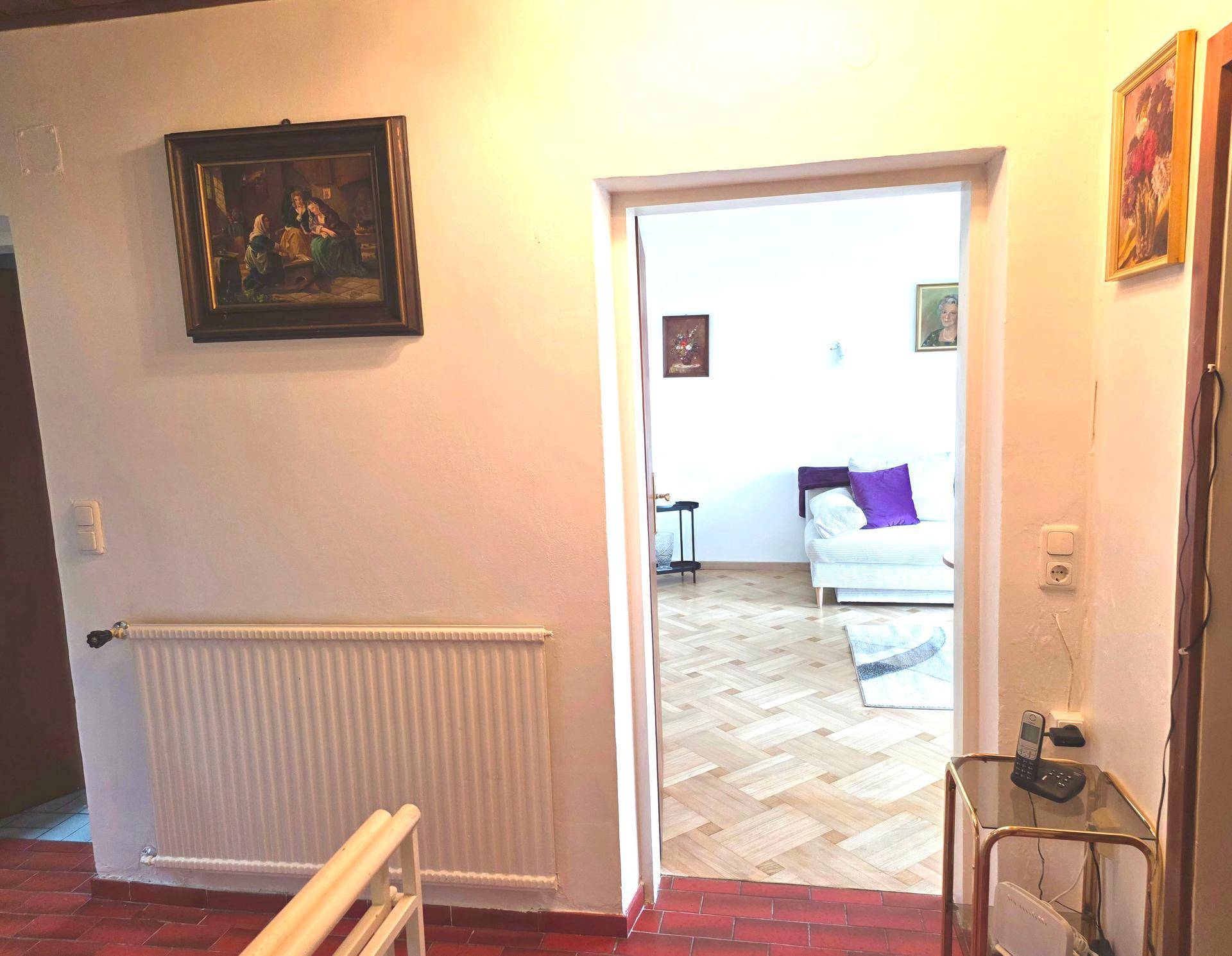 Flur mit Terrakotta-Fliesenboden und Blick in ein helles Wohnzimmer mit Parkett.