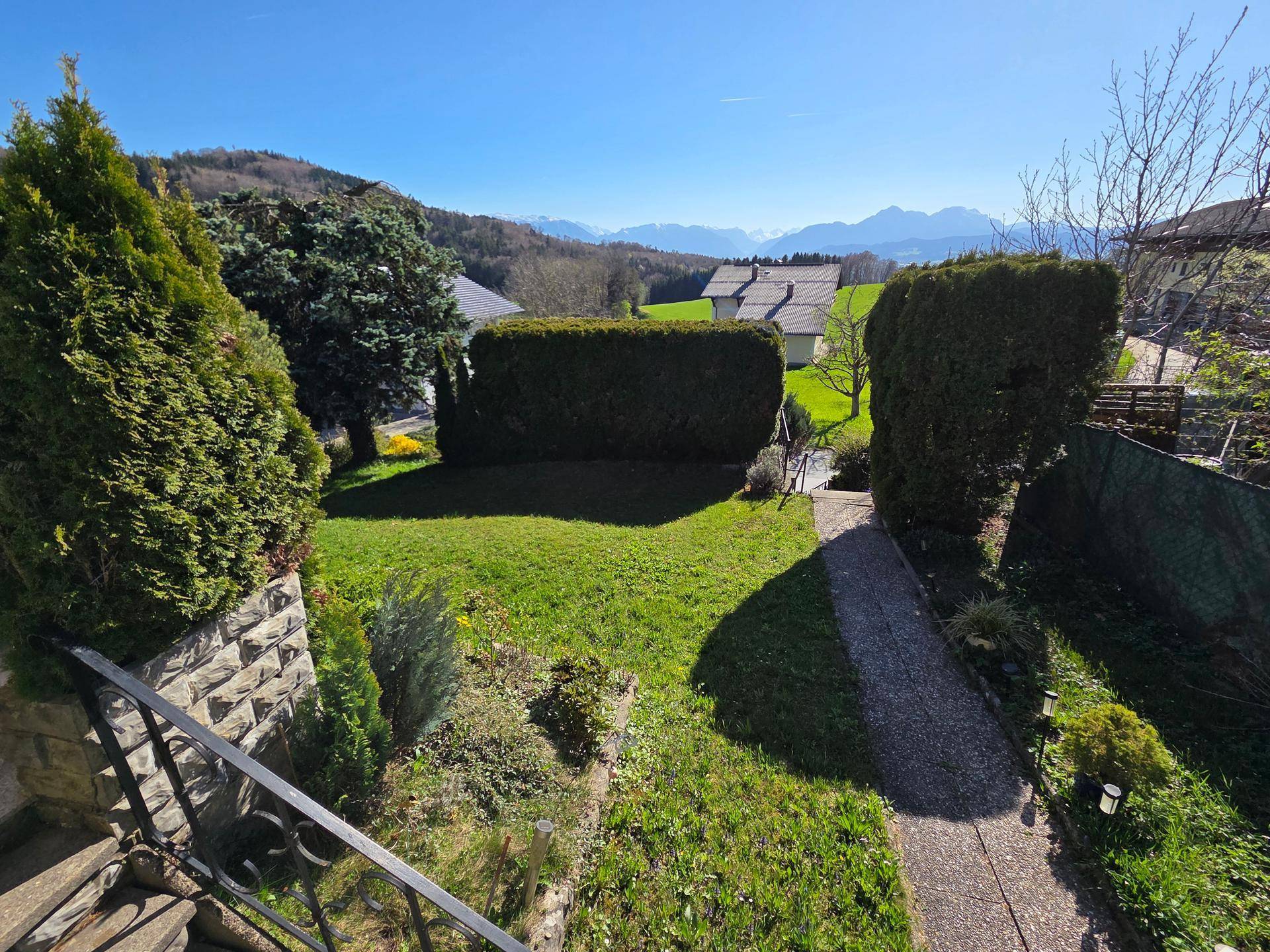 Sonniger Garten mit Rasenfläche und Panoramablick auf die Berge und grüne Umgebung.