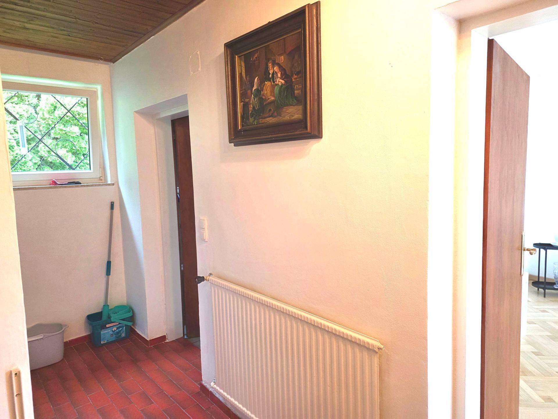 Eingangsbereich mit Terrakotta-Fliesenboden, Fenster und Heizkörper, mit Blick auf den Garten.