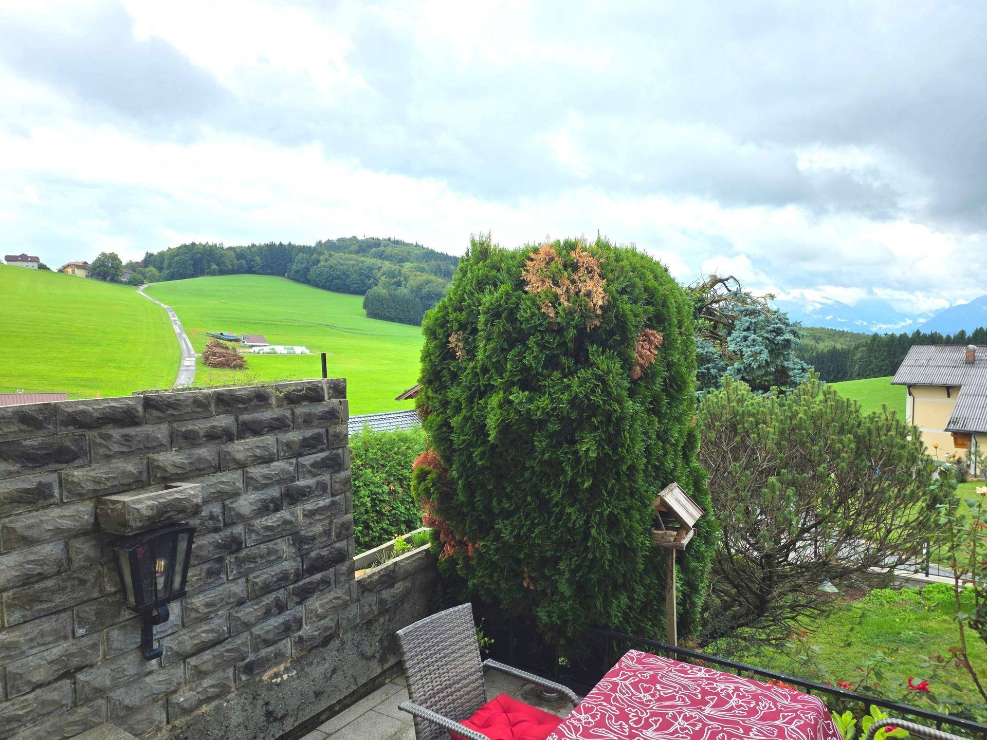 Terrasse mit Steinmauer und Sitzgelegenheiten, umgeben von üppigem Grün und weitem Landschaftsblick.