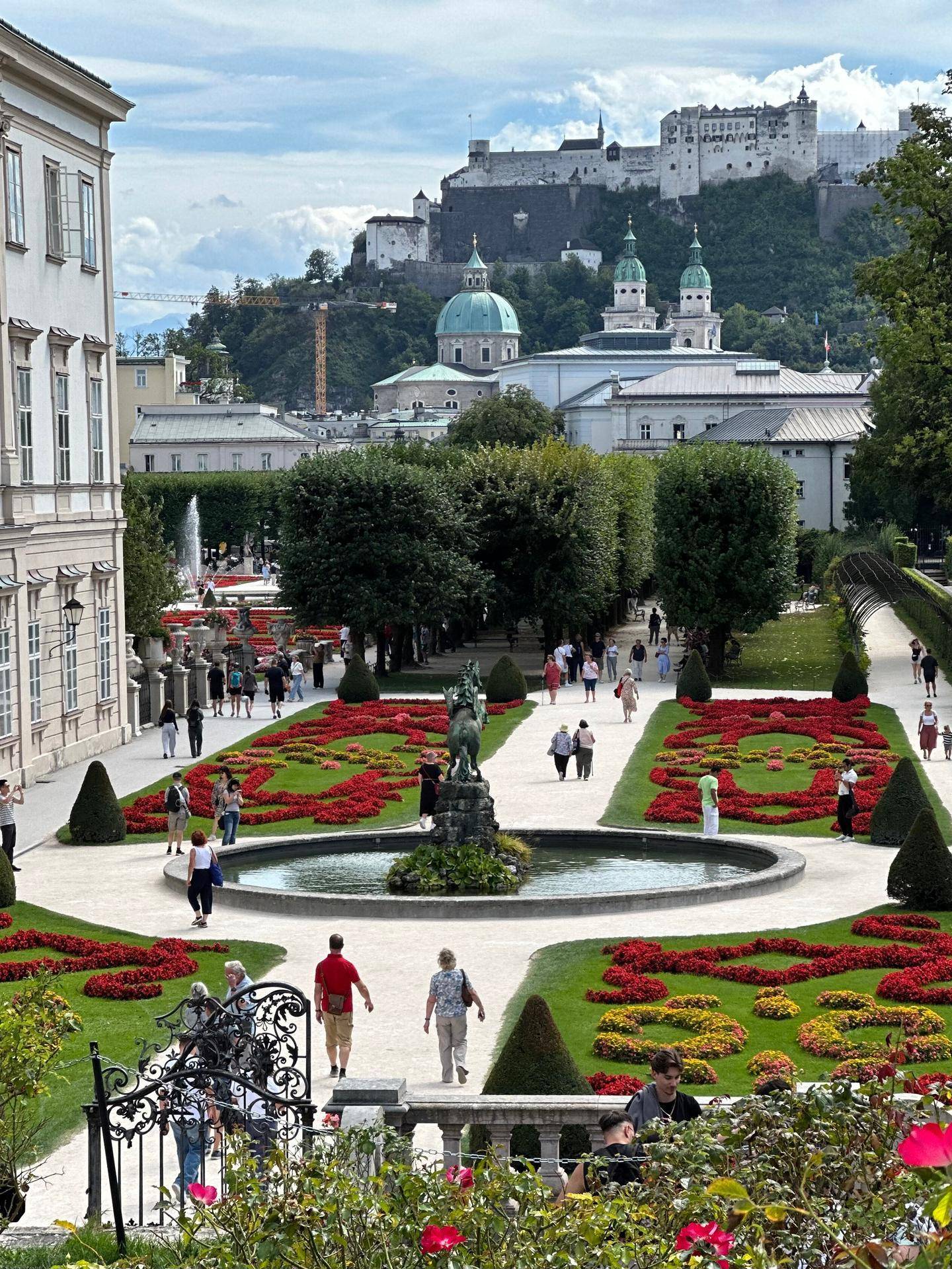 Historischer Garten mit Springbrunnen und Blumenbeeten, im Hintergrund die Festung Hohensalzburg.