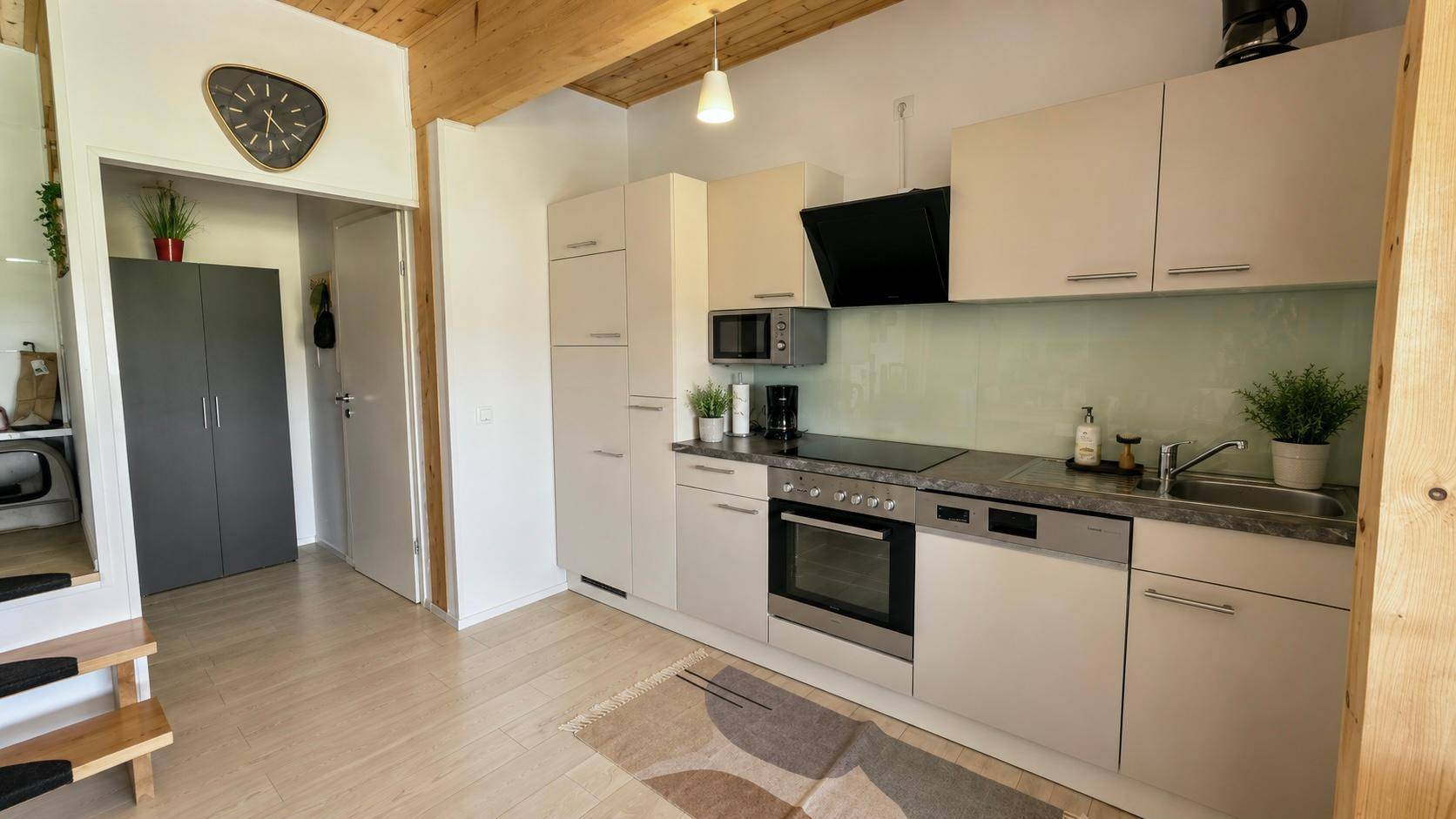 Moderne Einbauküche mit hellen Schränken, integrierten Geräten und Holzbalkendecke.