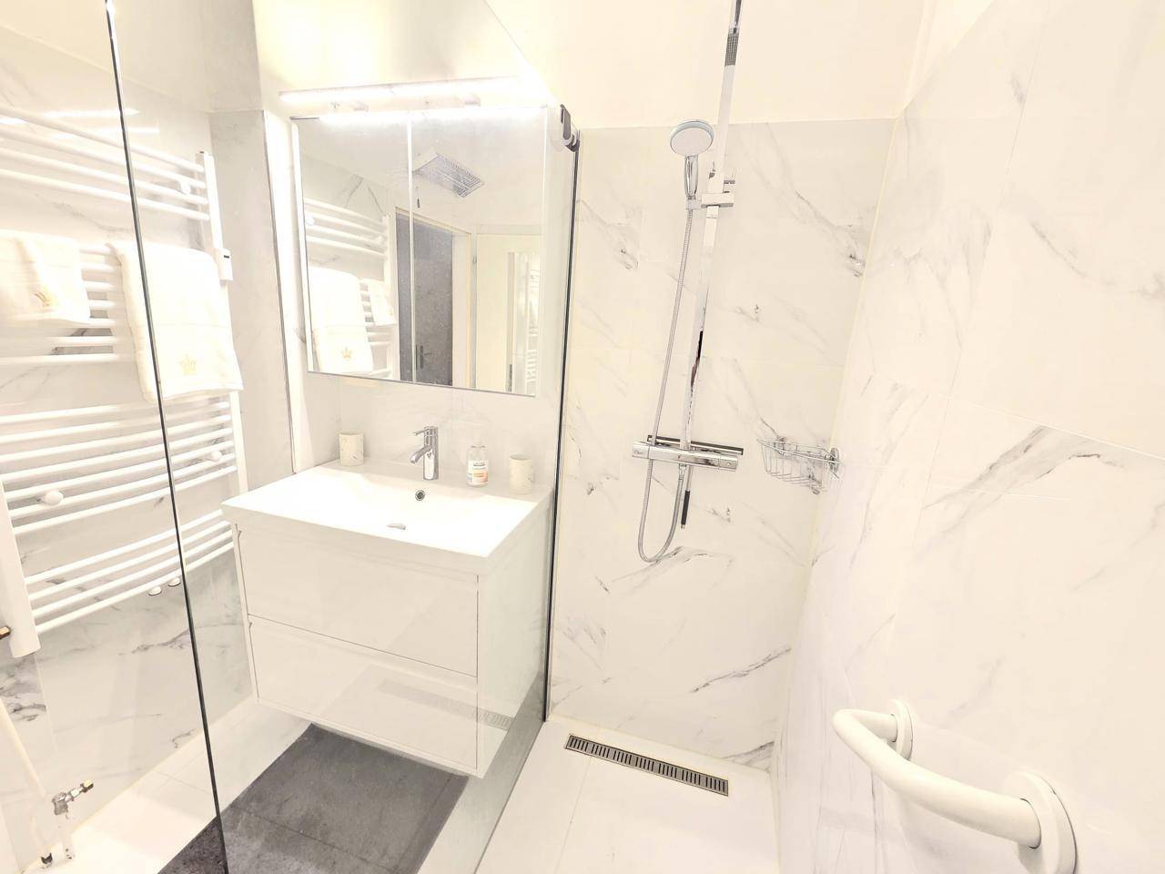 Modernes Badezimmer mit ebenerdiger Dusche, Marmoroptik-Fliesen und beheiztem Handtuchhalter.