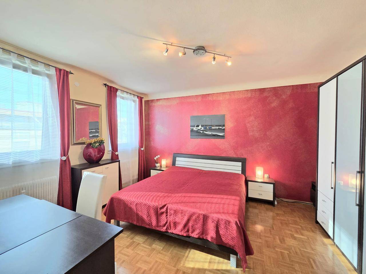 Gemütliches Schlafzimmer mit roter Akzentwand, Doppelbett und weißem Kleiderschrank.