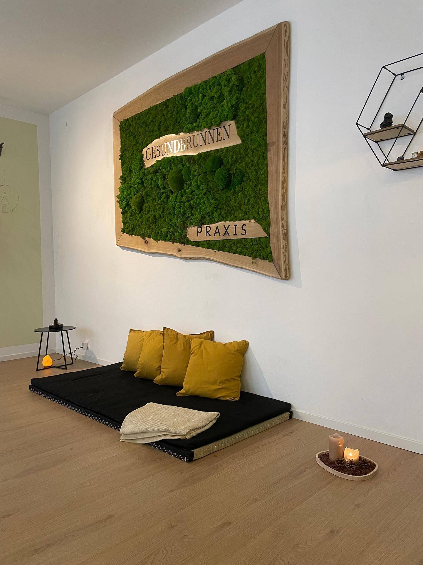 Ruhiger Raum mit Bodenmatratze, gelben Kissen und einem dekorativen Moosbild an der Wand.