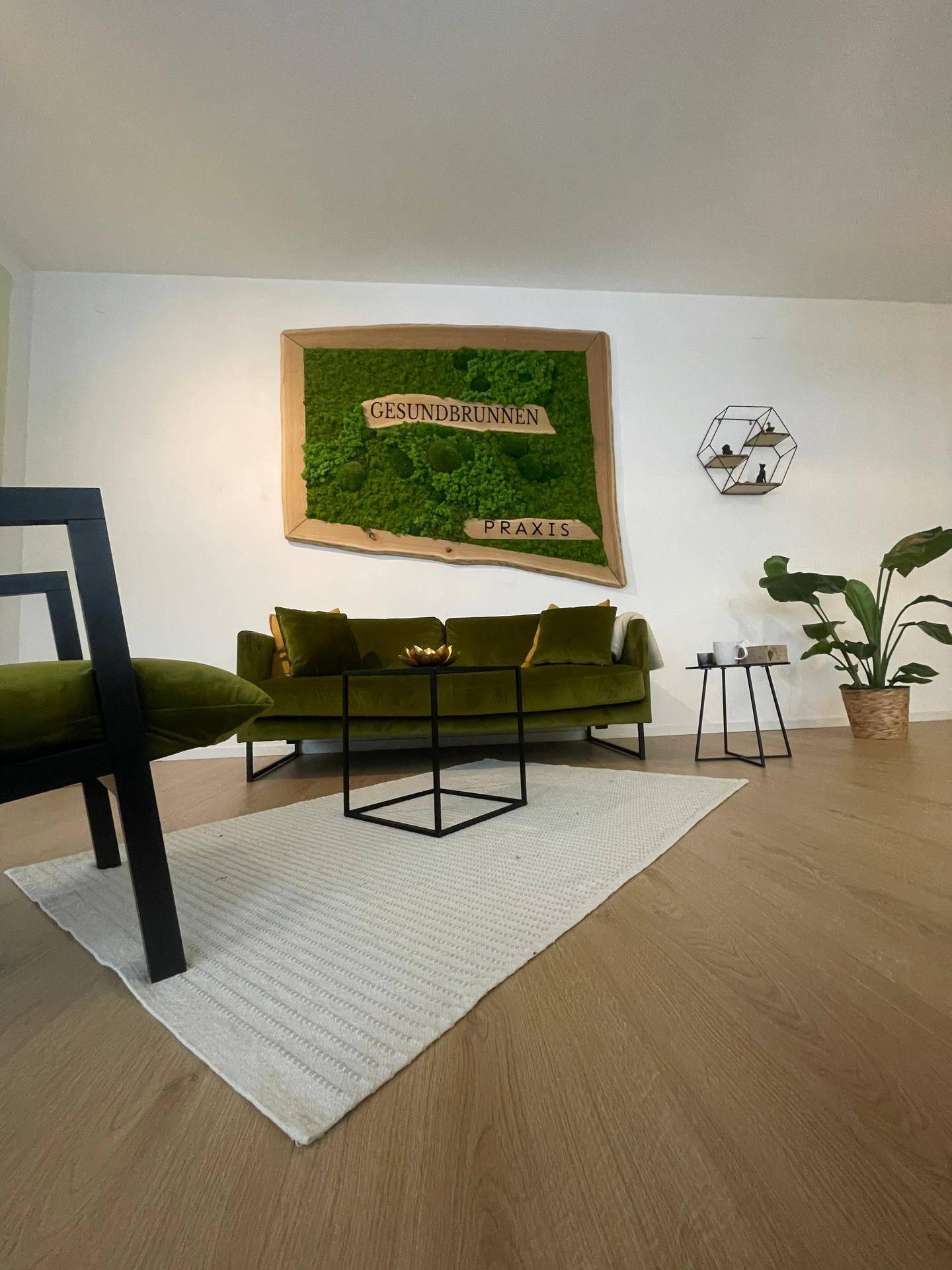 Gemütlicher Wartebereich mit olivgrünem Sofa, Holzboden und einem großen Moosbild an der Wand.