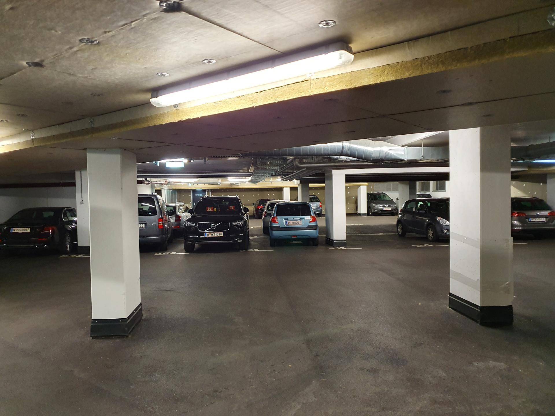 Geräumige Tiefgarage mit vielen Stellplätzen und sichtbaren Deckeninstallationen und Säulen.