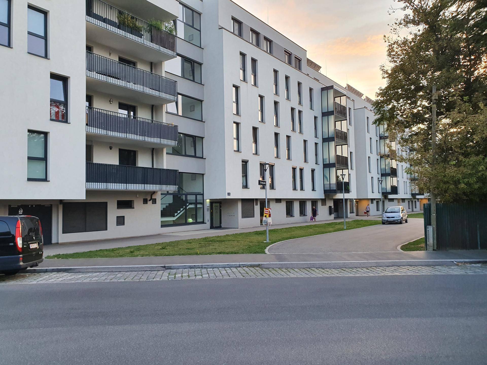 Moderne Wohnanlage mit weißen Fassaden, Balkonen und großen Fenstern bei Sonnenuntergang.