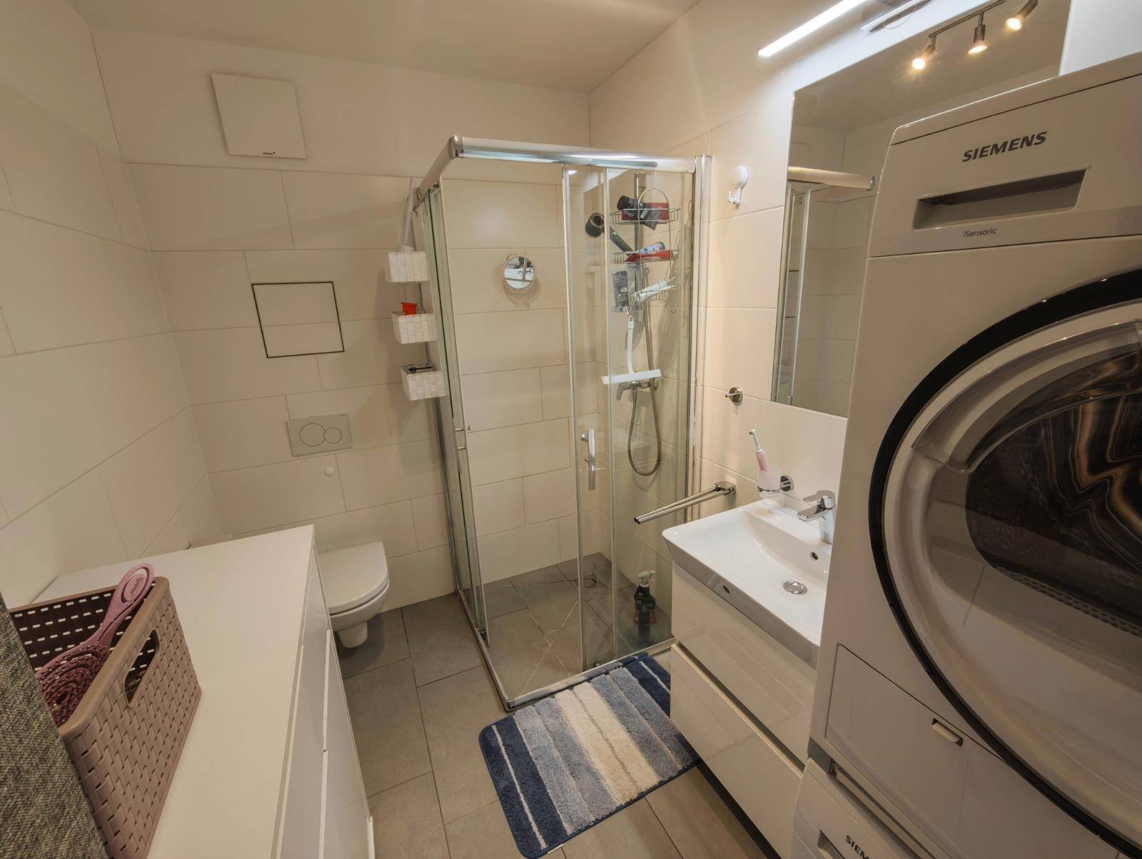Funktionales Badezimmer mit Duschkabine, Waschbecken und Waschmaschine/Trockner-Turm.