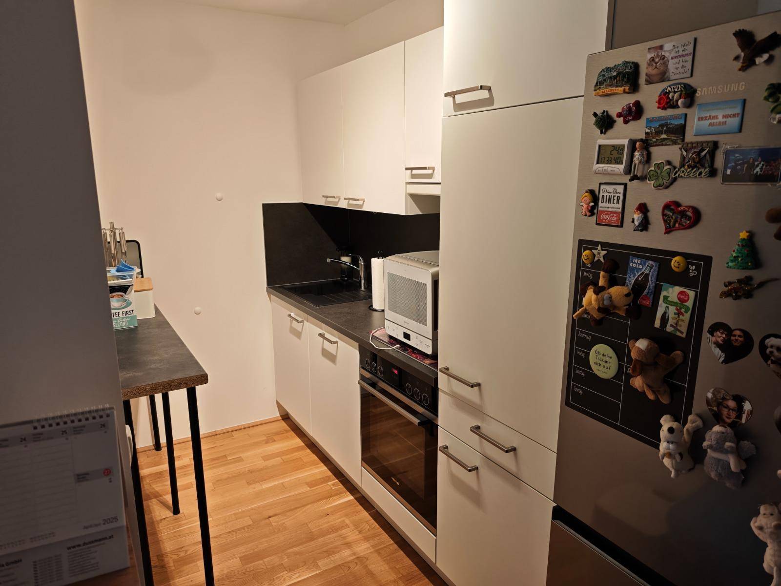 Kleine, moderne Küche mit weißen Schränken, schwarzer Arbeitsplatte und Einbaugeräten.