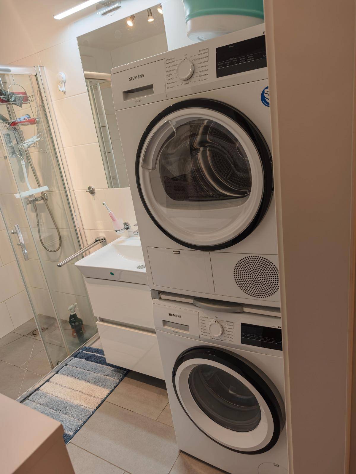 Badezimmer mit gestapelter Waschmaschine und Trockner sowie Duschkabine.