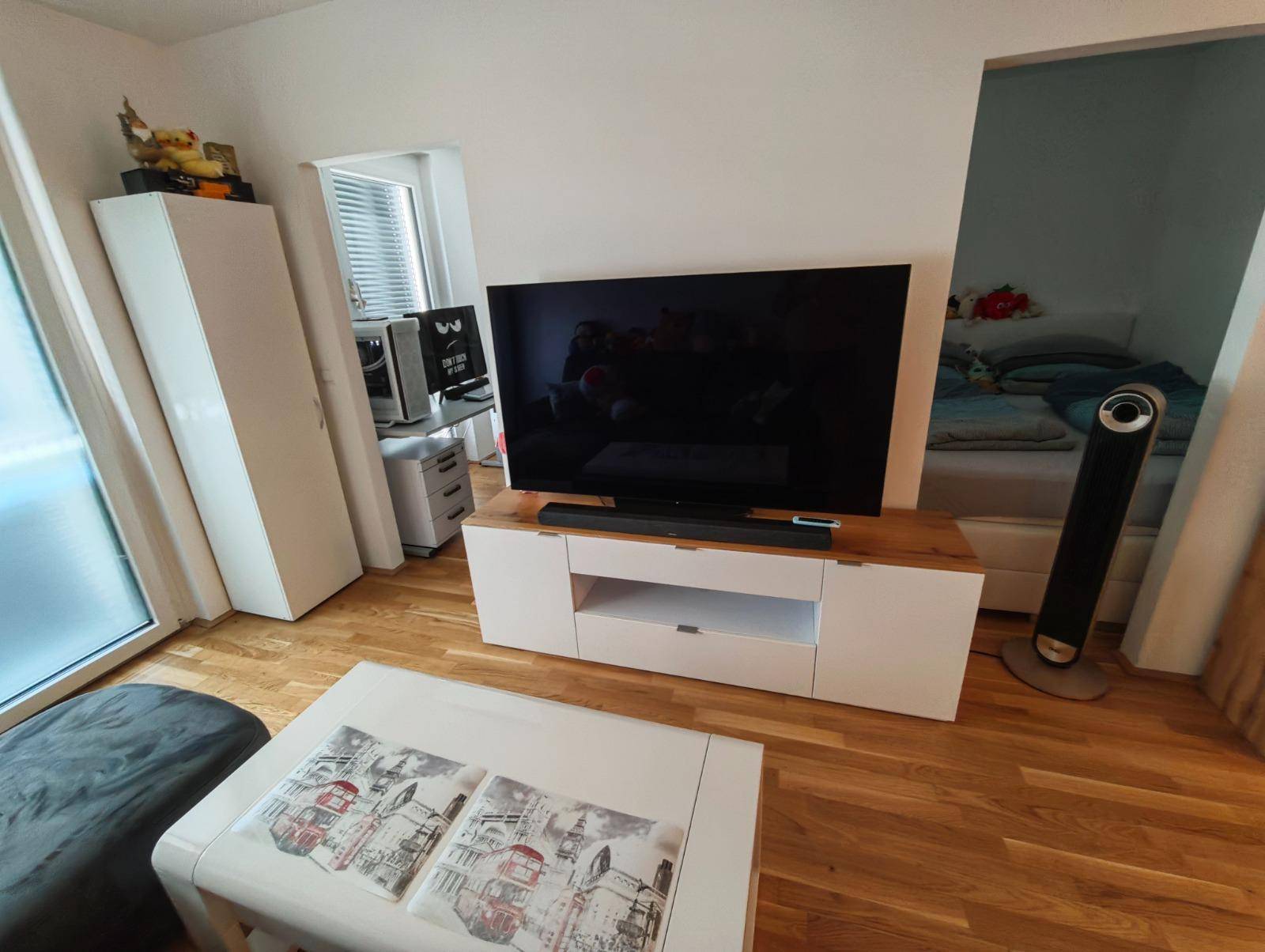 Wohnzimmer mit großem Fernseher und Blick in das angrenzende Schlafzimmer.