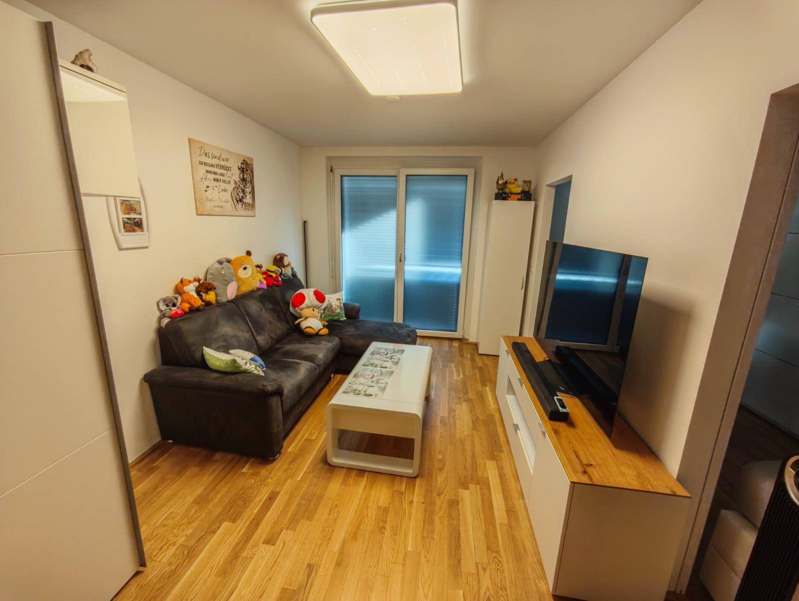 Wohnzimmer mit Sofa, Fernseher und Zugang zu einem Balkon oder einer Terrasse.