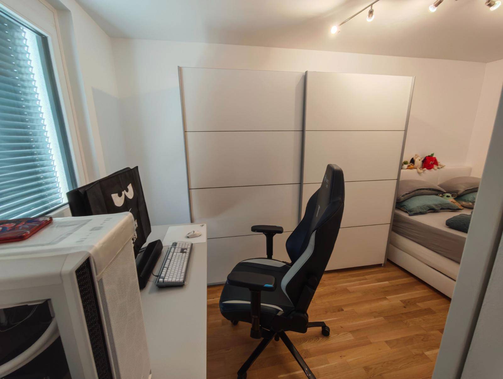 Schlafzimmer mit Holzboden, großem Kleiderschrank und Arbeitsbereich am Fenster.