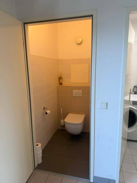 Separates WC mit wandhängender Toilette und hellen Fliesen an den Wänden.