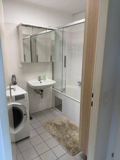 Badezimmer mit Badewanne, Duschwand, Waschbecken, Spiegelschrank und Waschmaschine.
