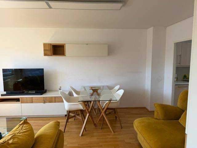 Gemütlicher Wohn-Essbereich mit gelbem Sofa, modernem Glastisch und hellem Parkettboden.