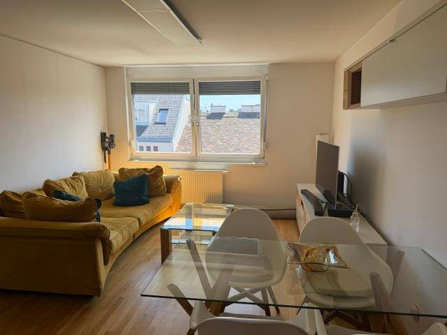 Wohnbereich mit Fensterblick auf die Dächer, gelbem Sofa und Esstisch für vier Personen.