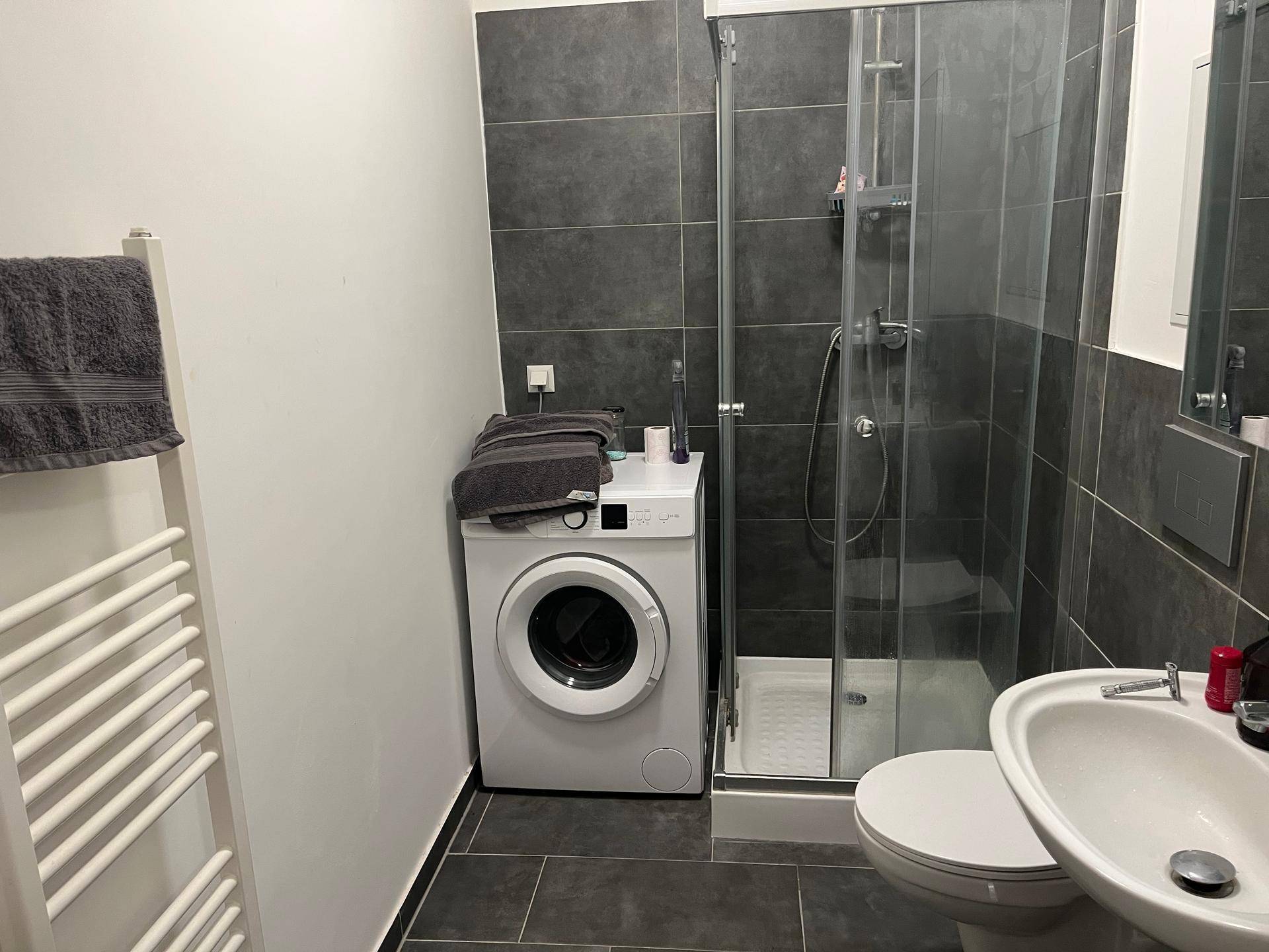 Modernes Badezimmer mit Duschkabine, Waschmaschine und dunklen Fliesen.