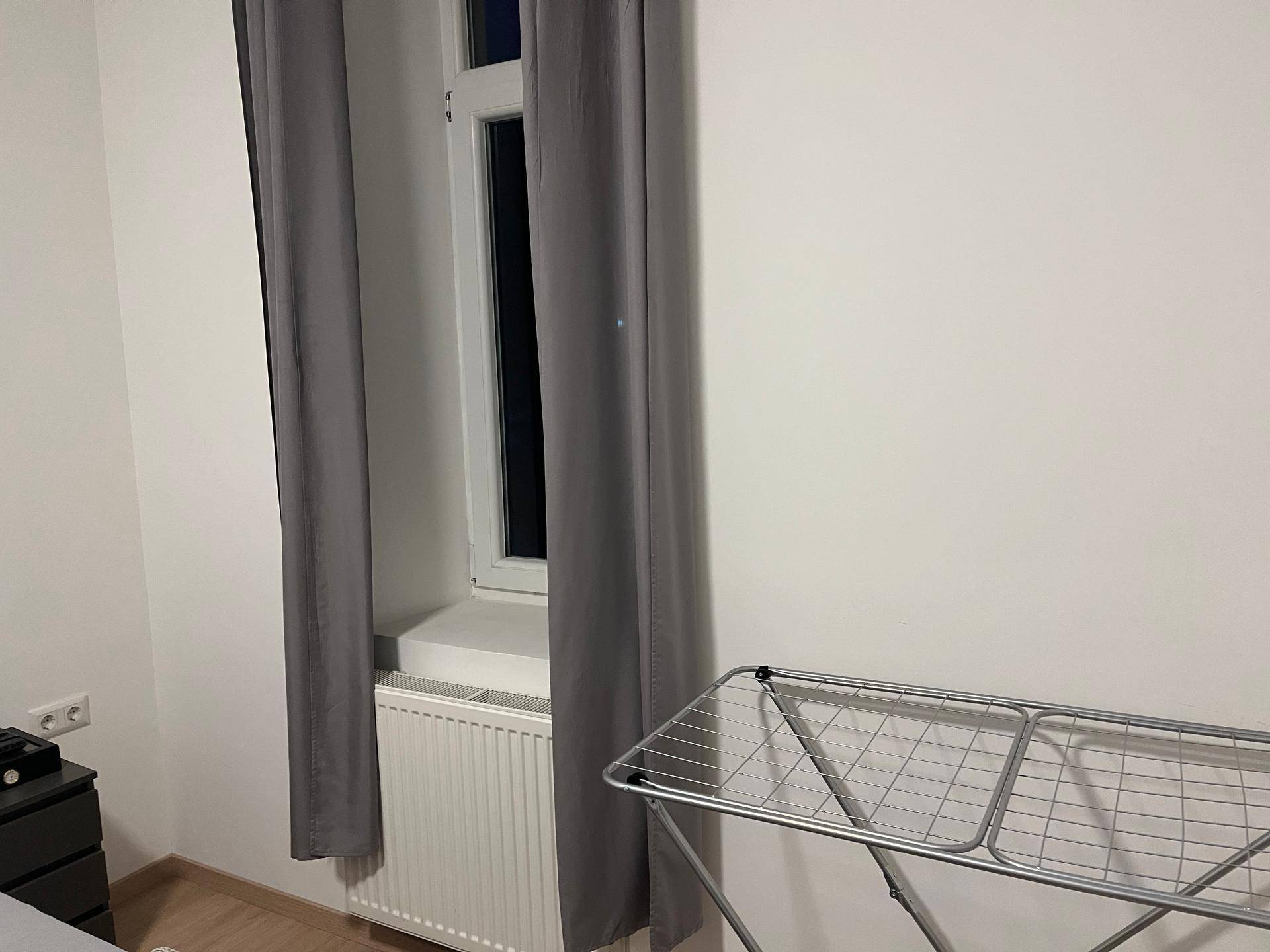 Fensterbereich mit Heizkörper und einem Wäscheständer in einem hellen Raum.