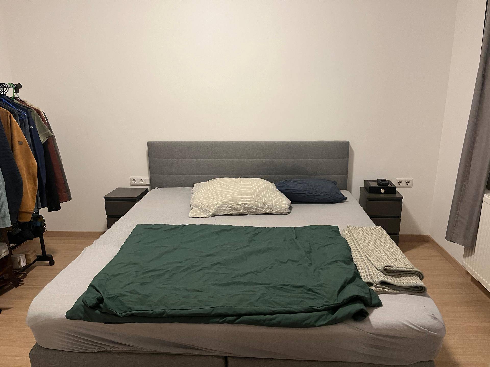 Schlafzimmer mit einem Doppelbett, Nachttischen und einem Kleiderständer.