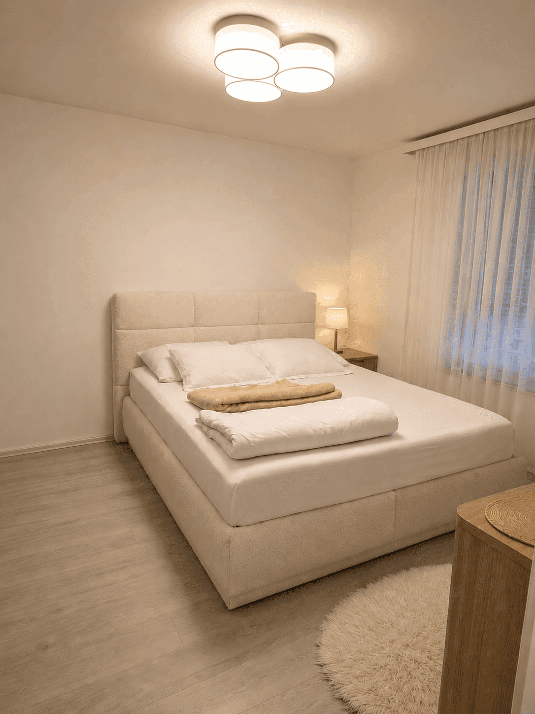 Gemütliches Schlafzimmer mit hellem Doppelbett, Nachttisch und weichen Textilien.