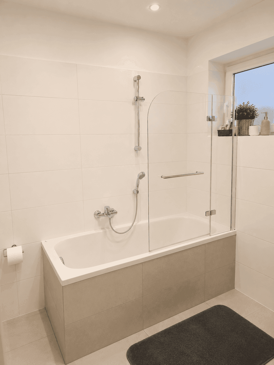 Helles Badezimmer mit Badewanne, Duschabtrennung und Fenster für Tageslicht.