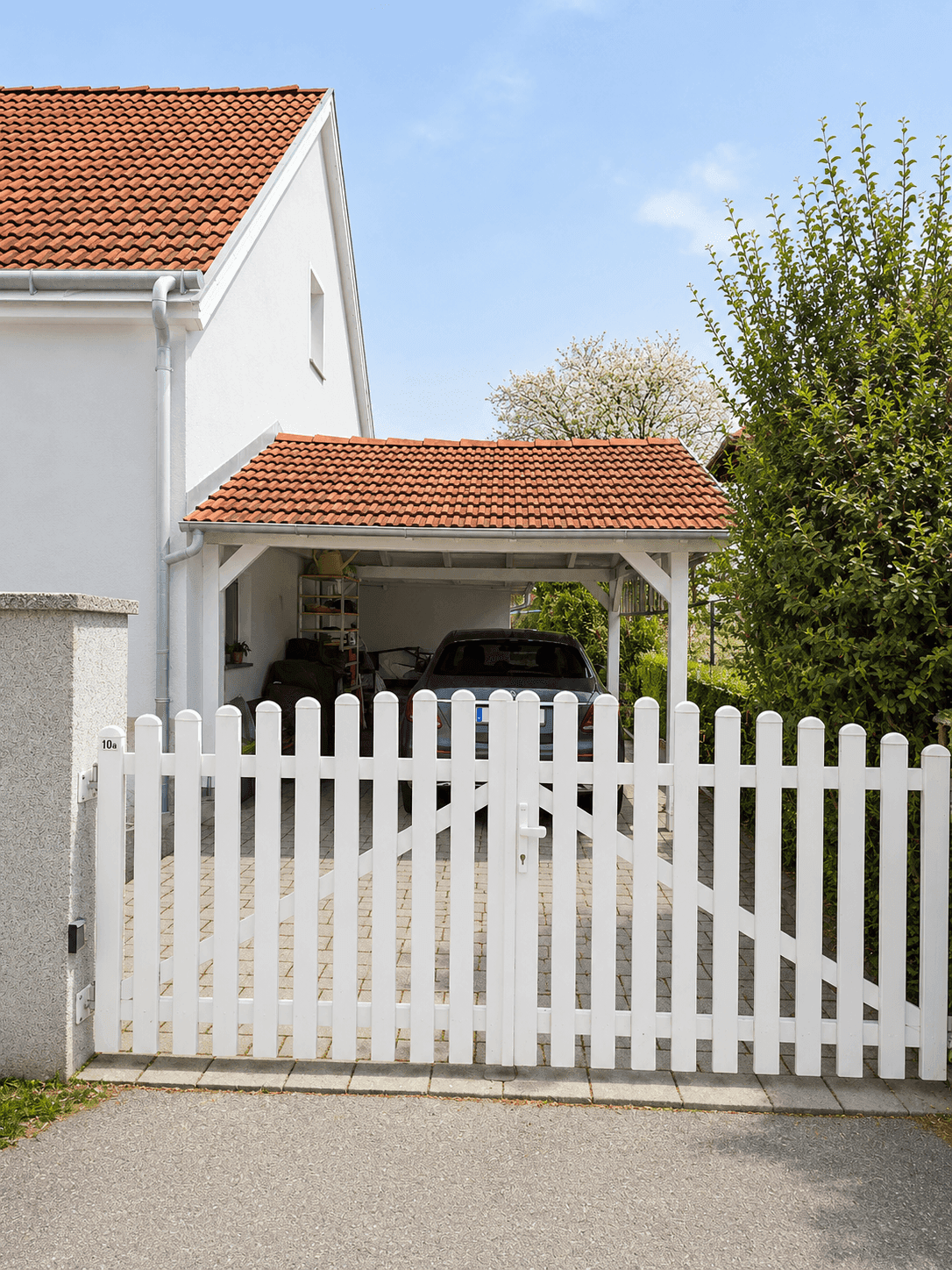 Überdachter Carport mit zwei Stellplätzen und weißem Lattenzaun vor dem Haus.