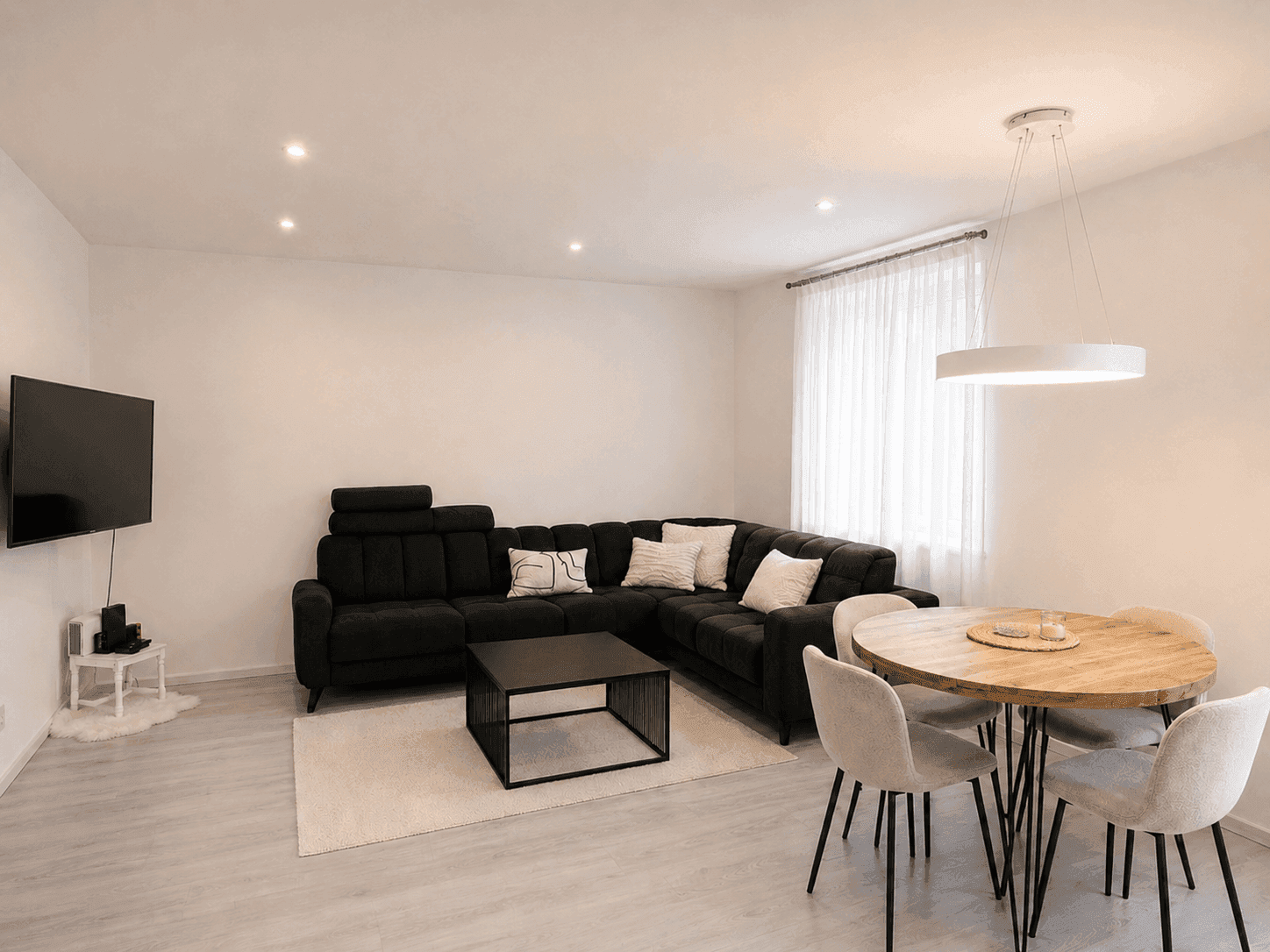 Moderner Wohn-Essbereich mit dunklem Ecksofa, hellem Teppich und Esstisch.