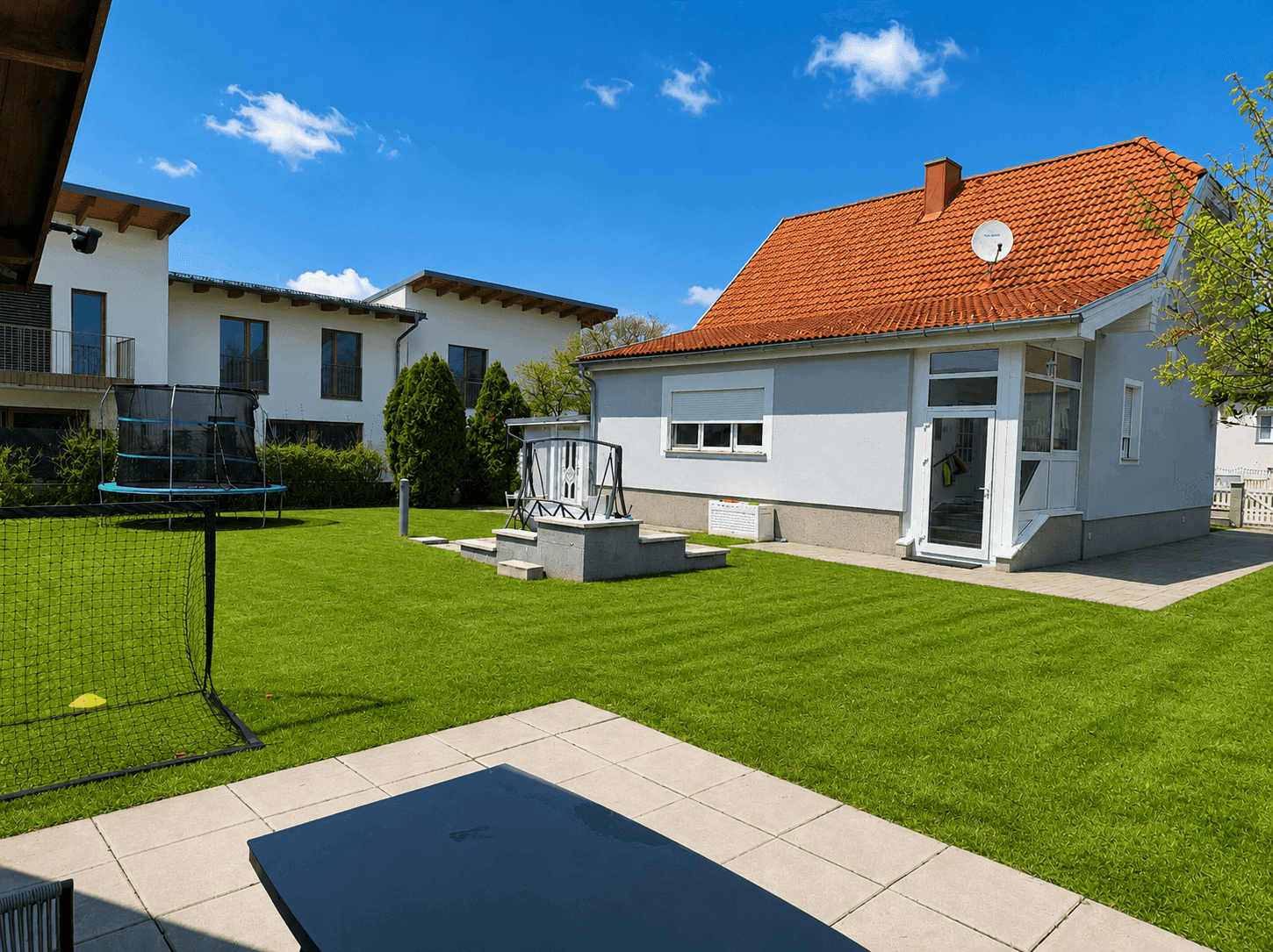 Gepflegter Garten mit großer Rasenfläche, Trampolin und Terrasse hinter dem Haus.