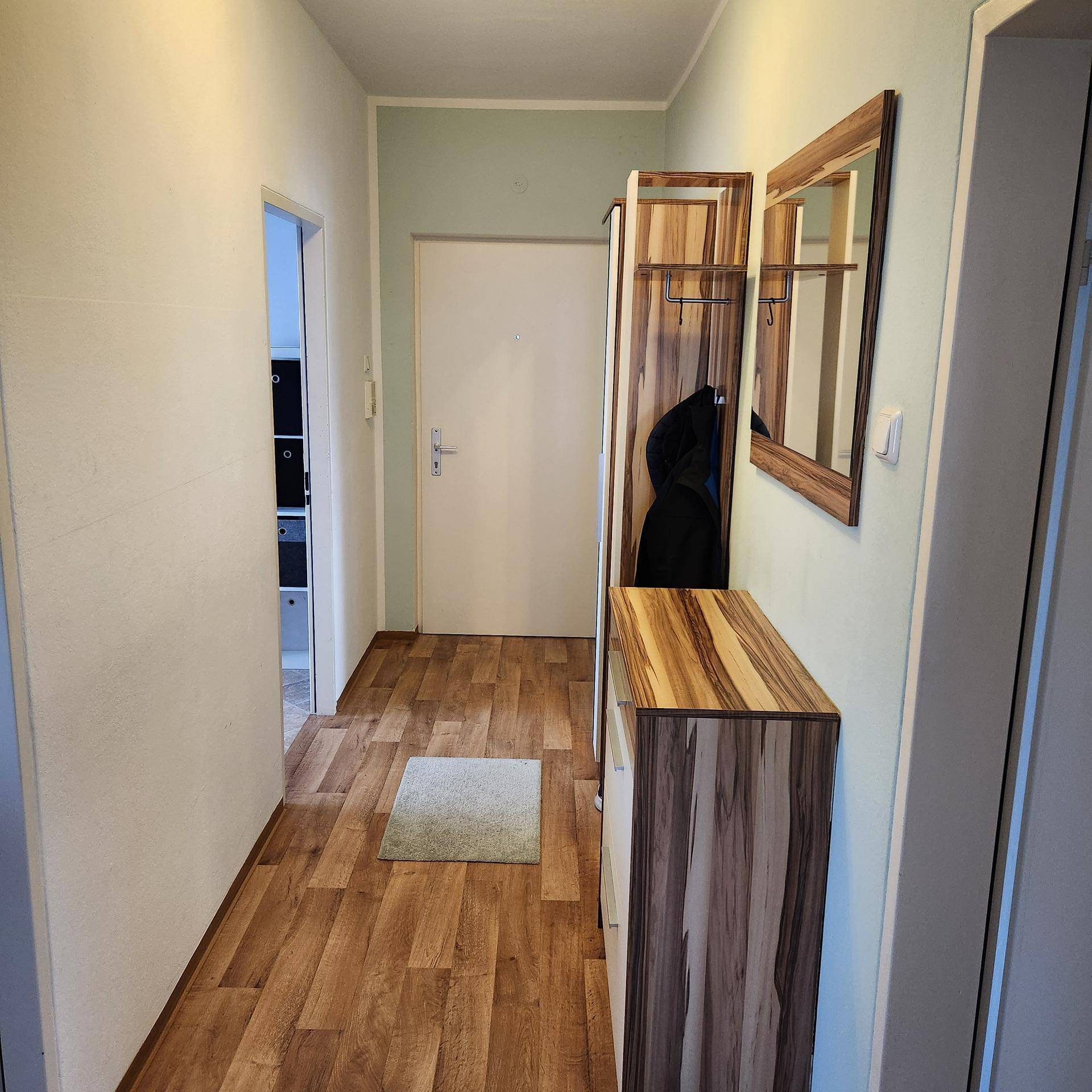 Heller Flur mit Holzoptikboden, Garderobe und einem Spiegel für den Eingangsbereich.