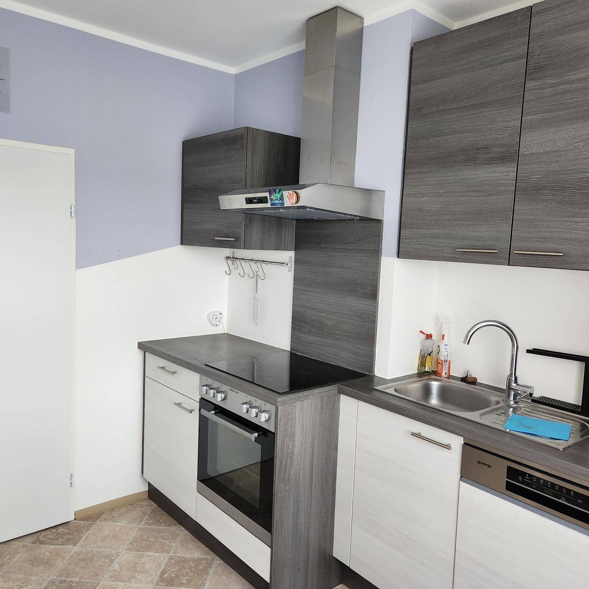 Moderne Küche mit grauen und weißen Schränken, Induktionskochfeld, Backofen und Dunstabzugshaube.
